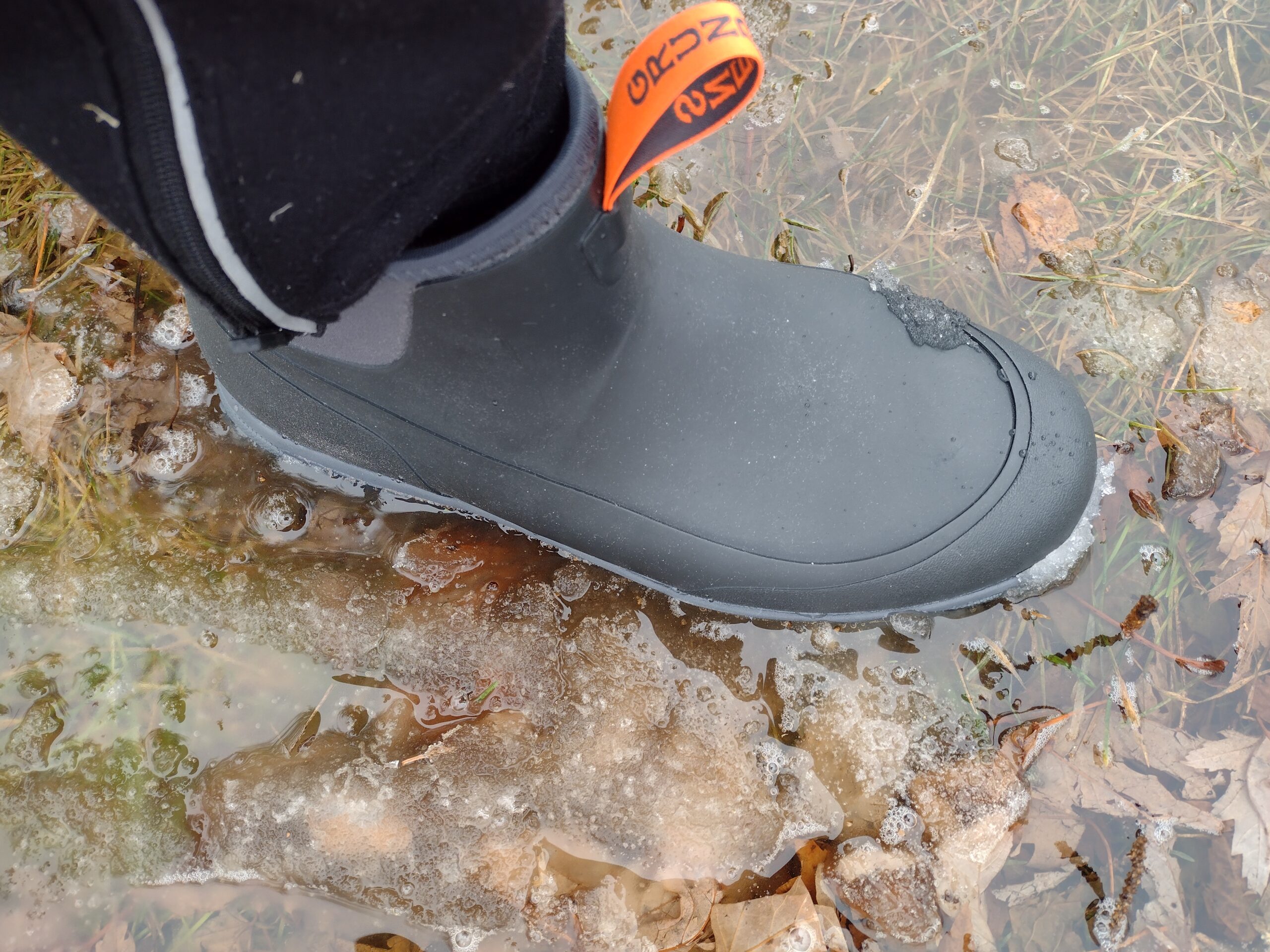 Ground level view of someone wearing the black Grundens Deviation Ankle Boot in icy water.