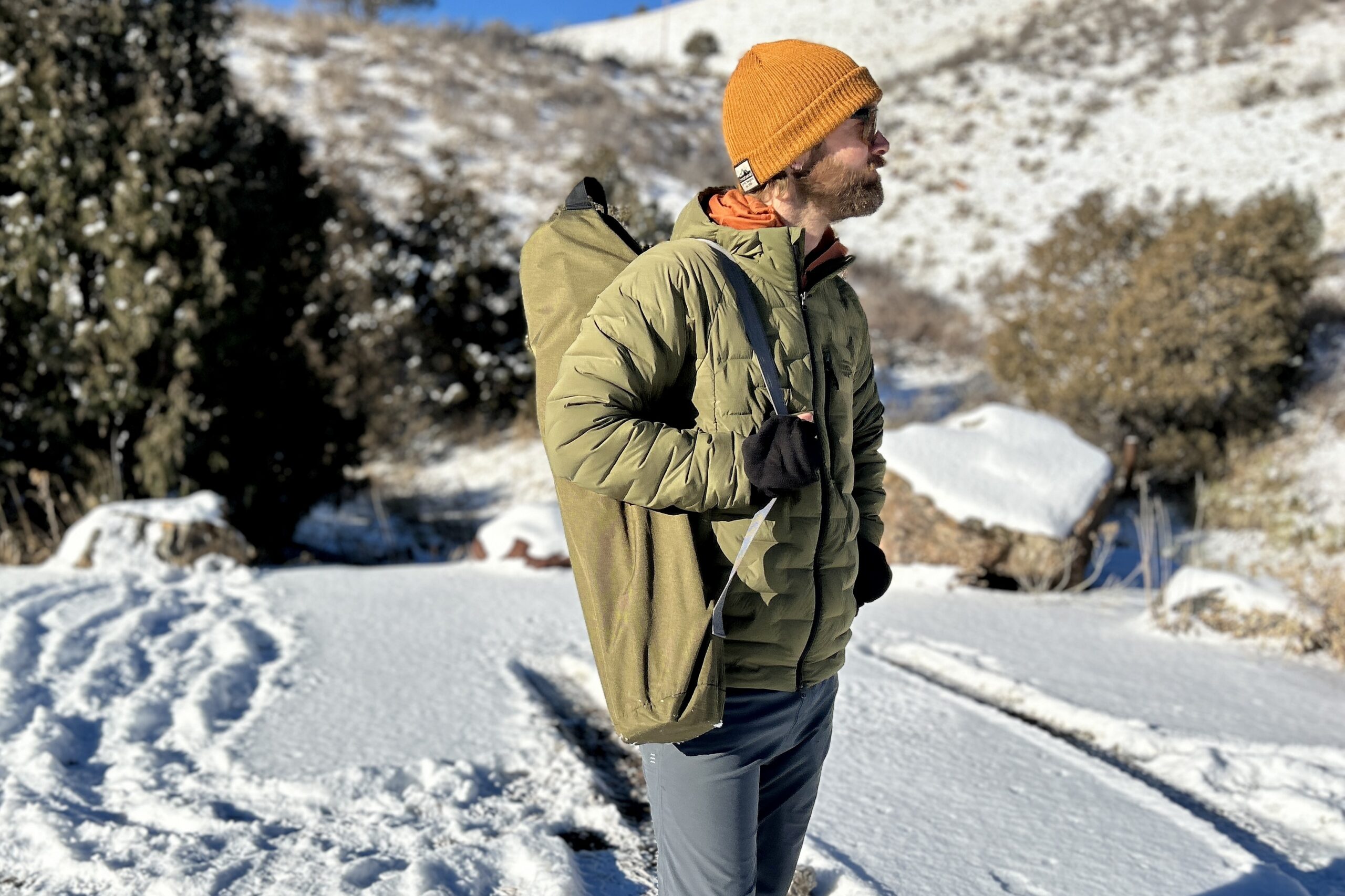 A man looks off in the distance with a camping chair slung over his shoulder on a snowy day.
