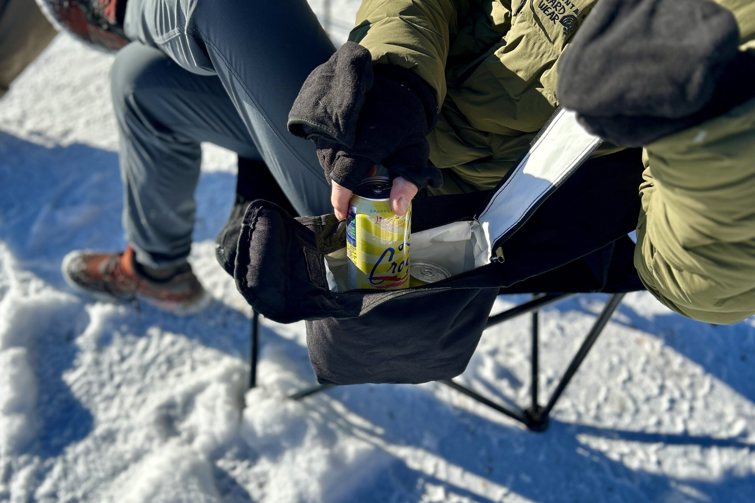 Close up of a person pulling out a can of drink from a pocket cooler on their camping chair.