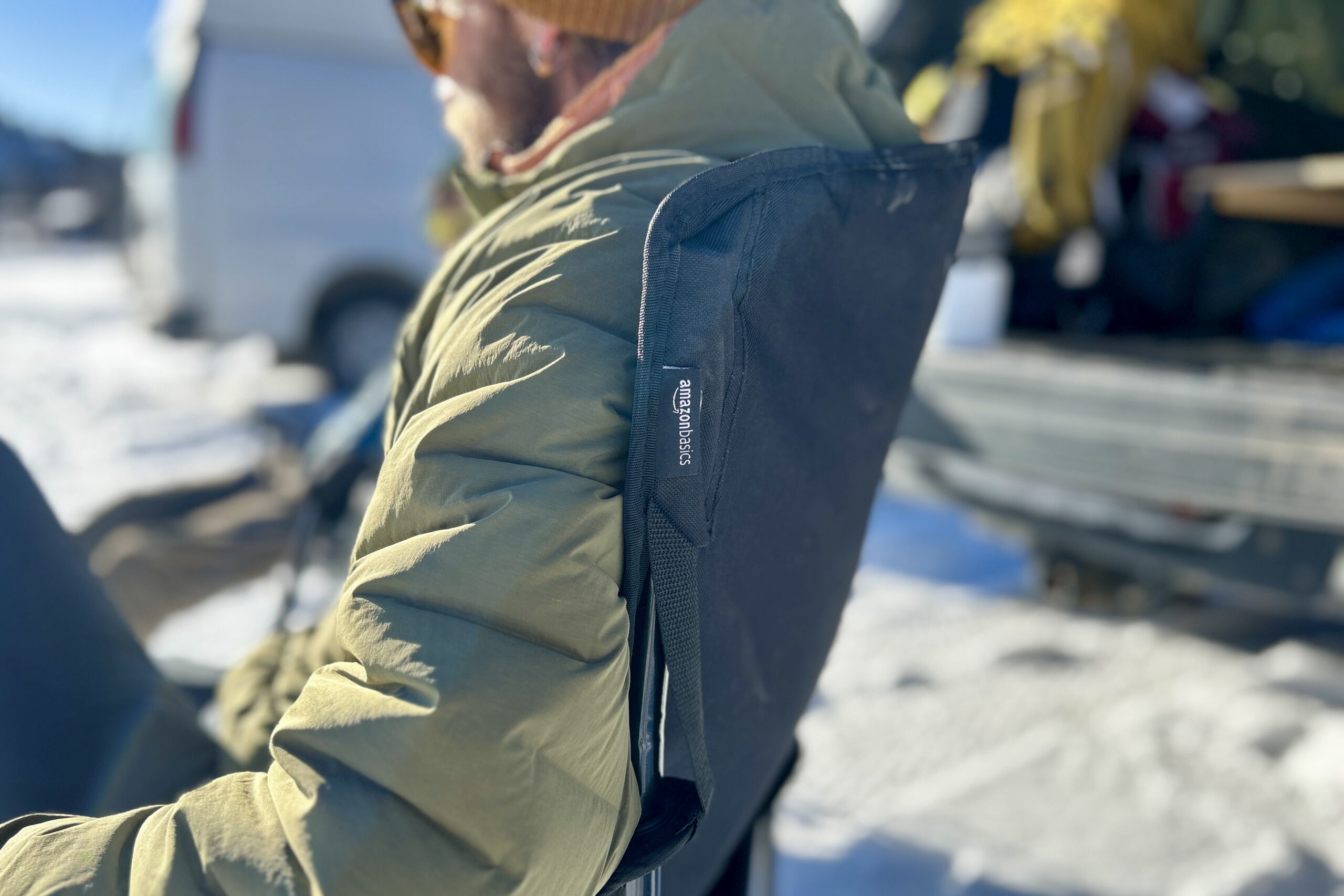 Close up side profile of the back of a camping chair with a person sitting in it, the logo visible on a small tag.