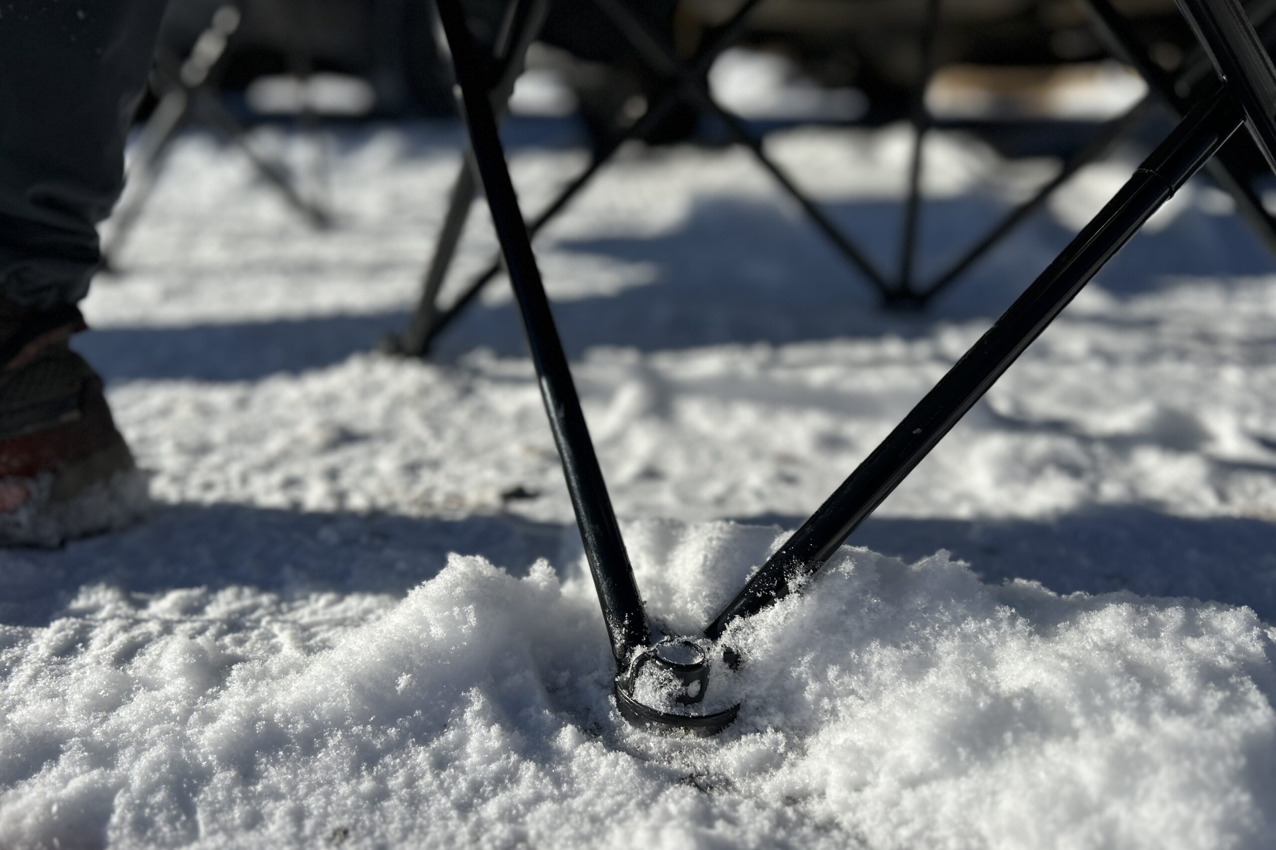 Close up of the feet and legs of a camping chair sitting on snowy ground.