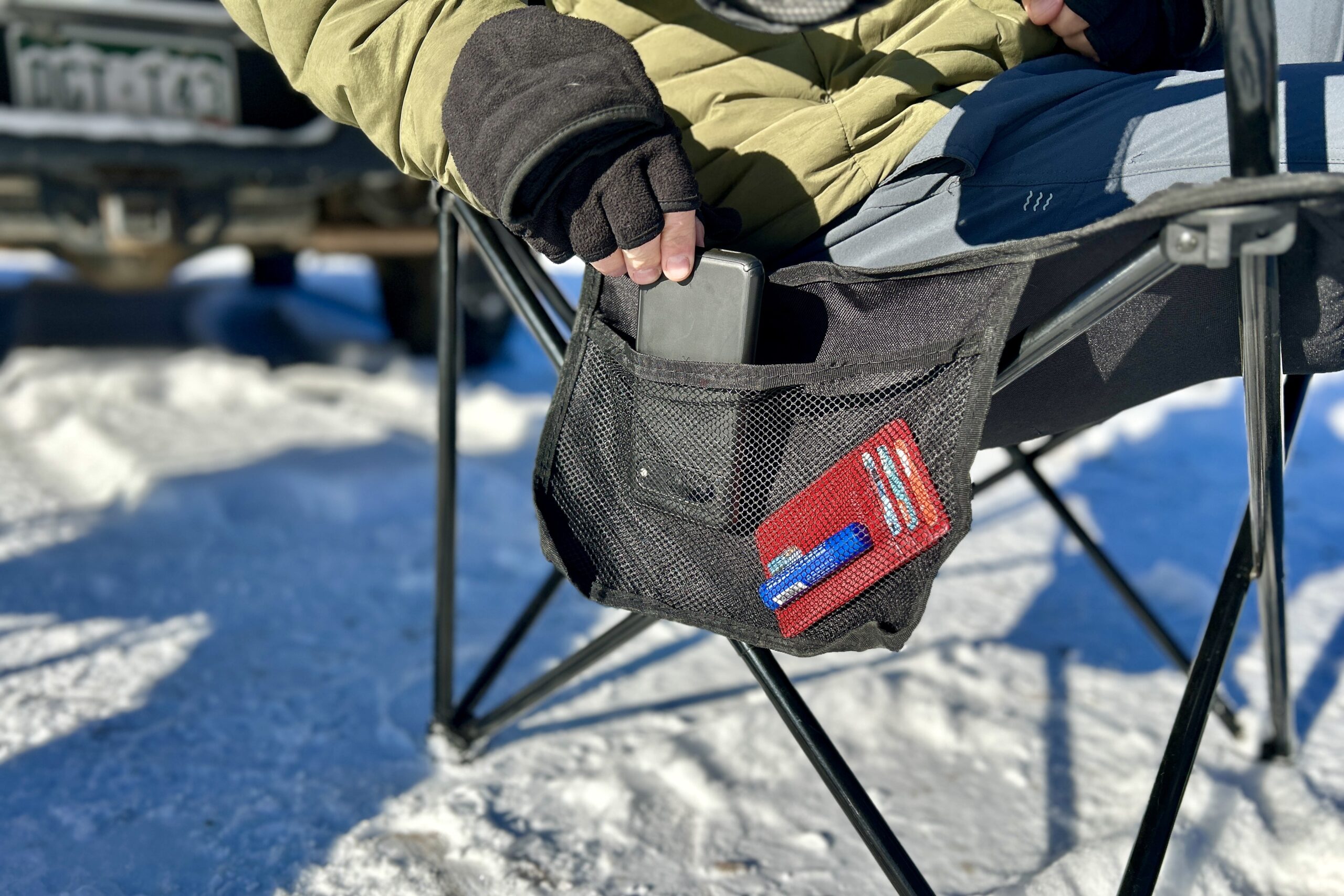 A person pulls their phone out of a mesh side pocket as they sit in a camping chair.