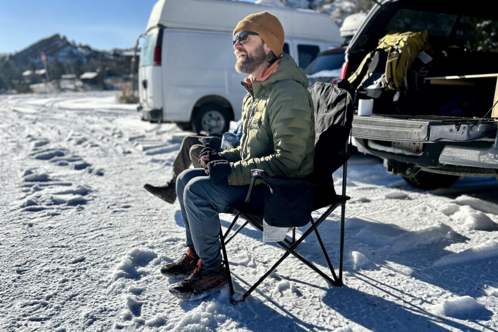 A man sits in a camping chair in a snowy parking lot.