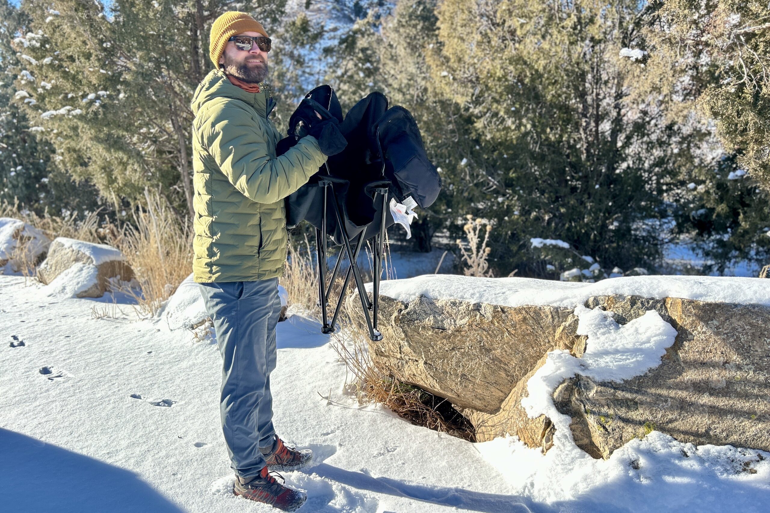 A man standing in a snowy place collapses a camping chair.