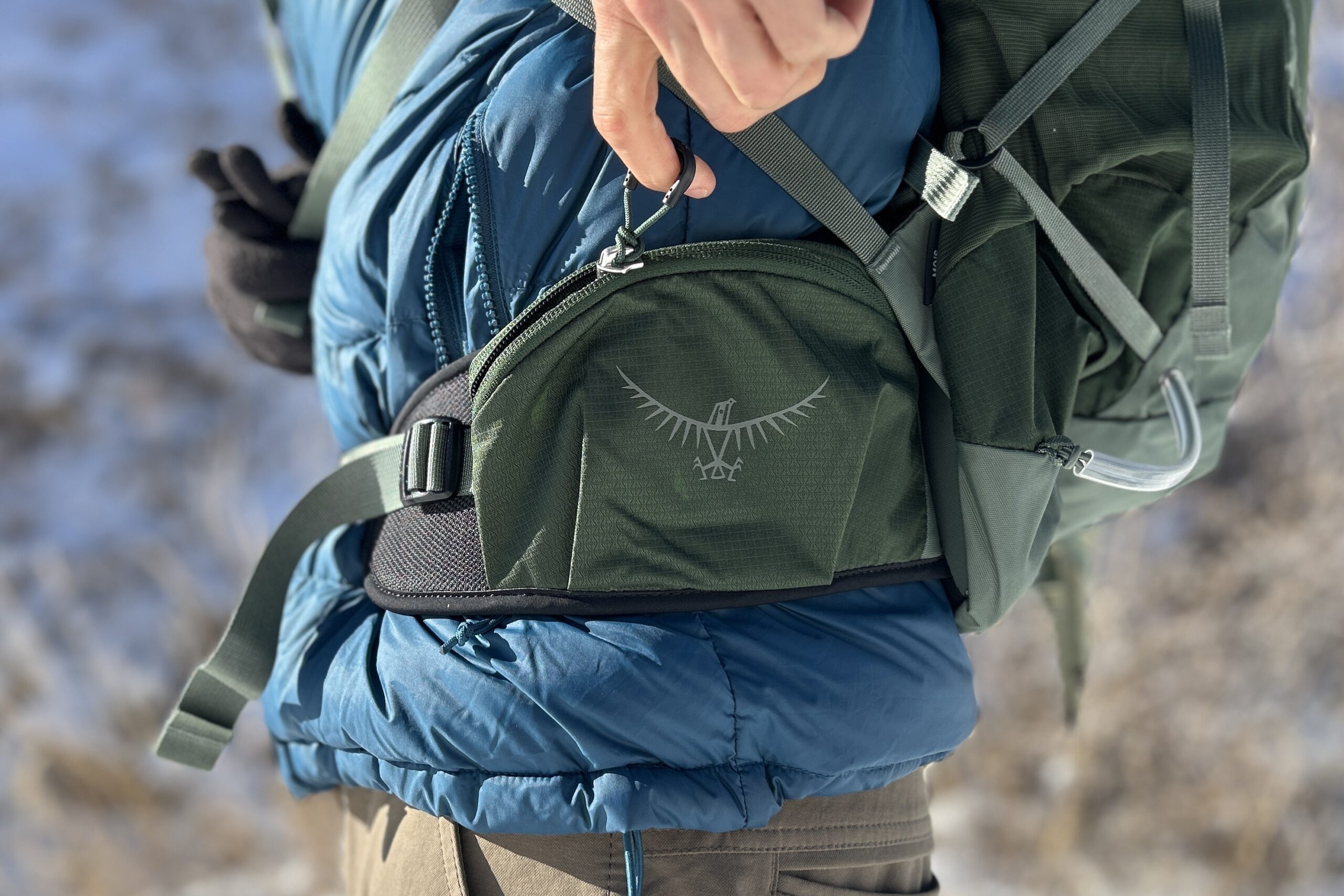 Close up of a person unzipping the wide waist strap pockets of a daypack.
