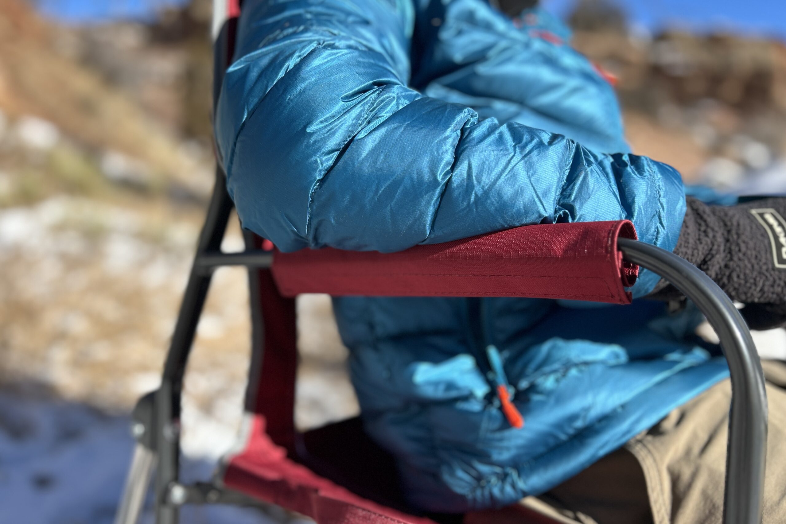 Close up of a person's elbows on the arm rests of a camping chair.