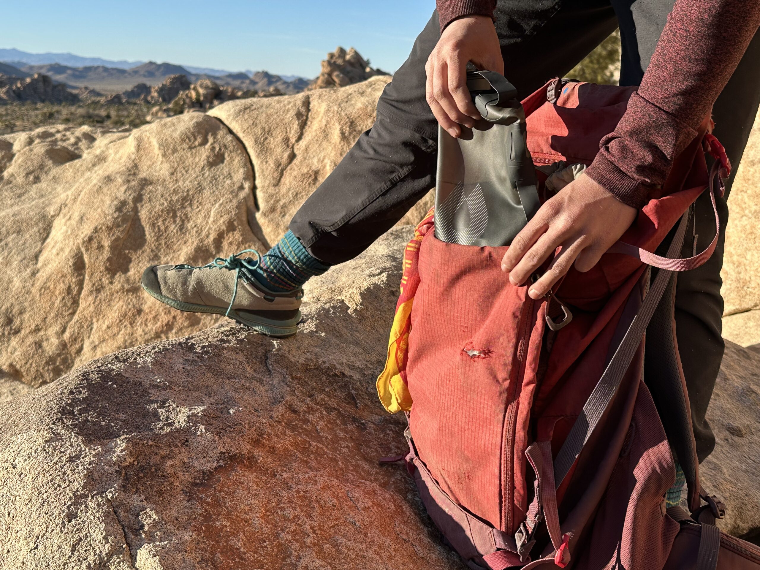 Close up of a hiker loading the HydraPak Seeker water bag into a red backpacking backpack. She is standing on a granite boulder in Joshua Tree National Park.