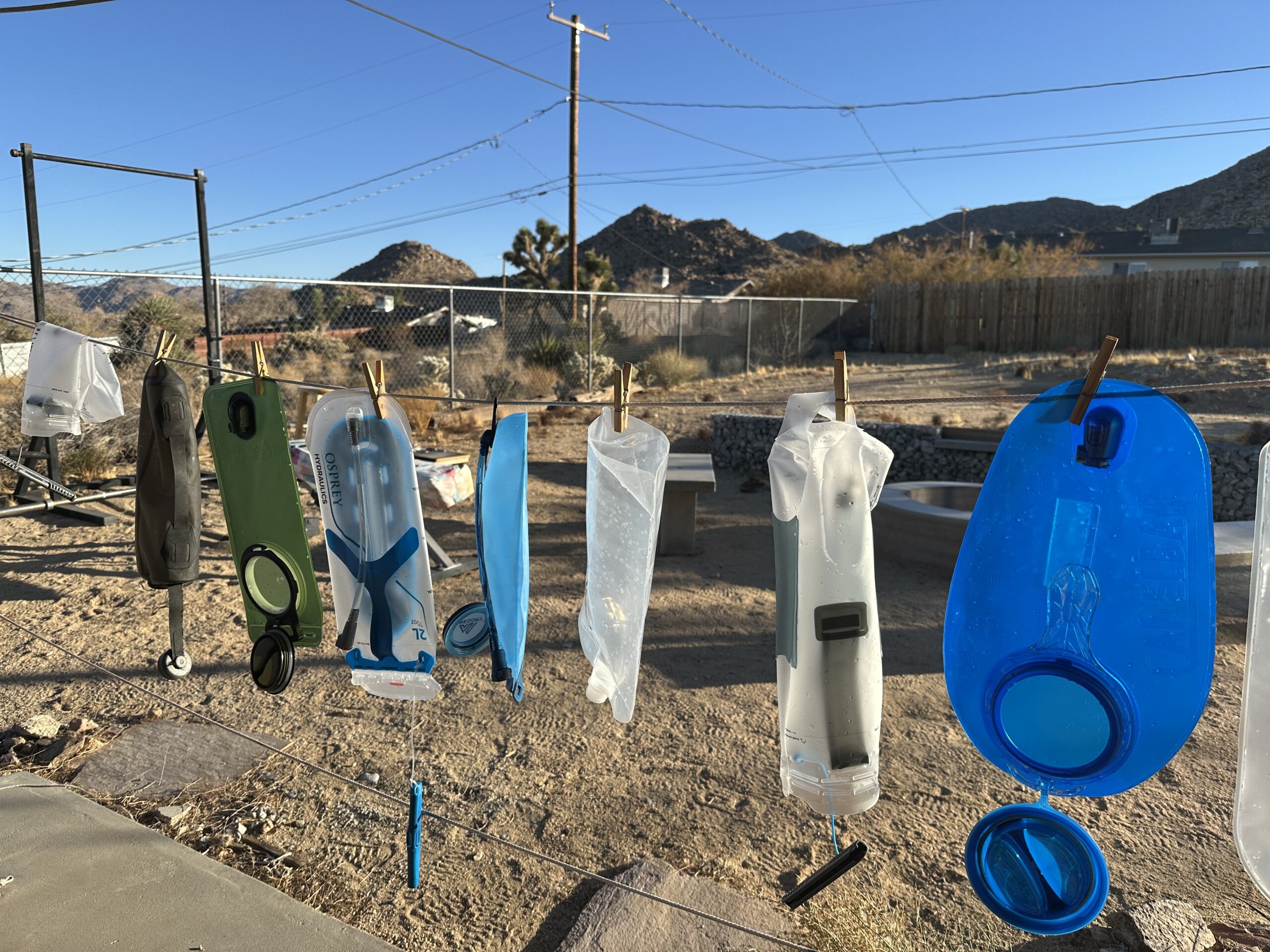 Image showing nine hydration bladders hanging to dry on a clothesline in a desert backyard.