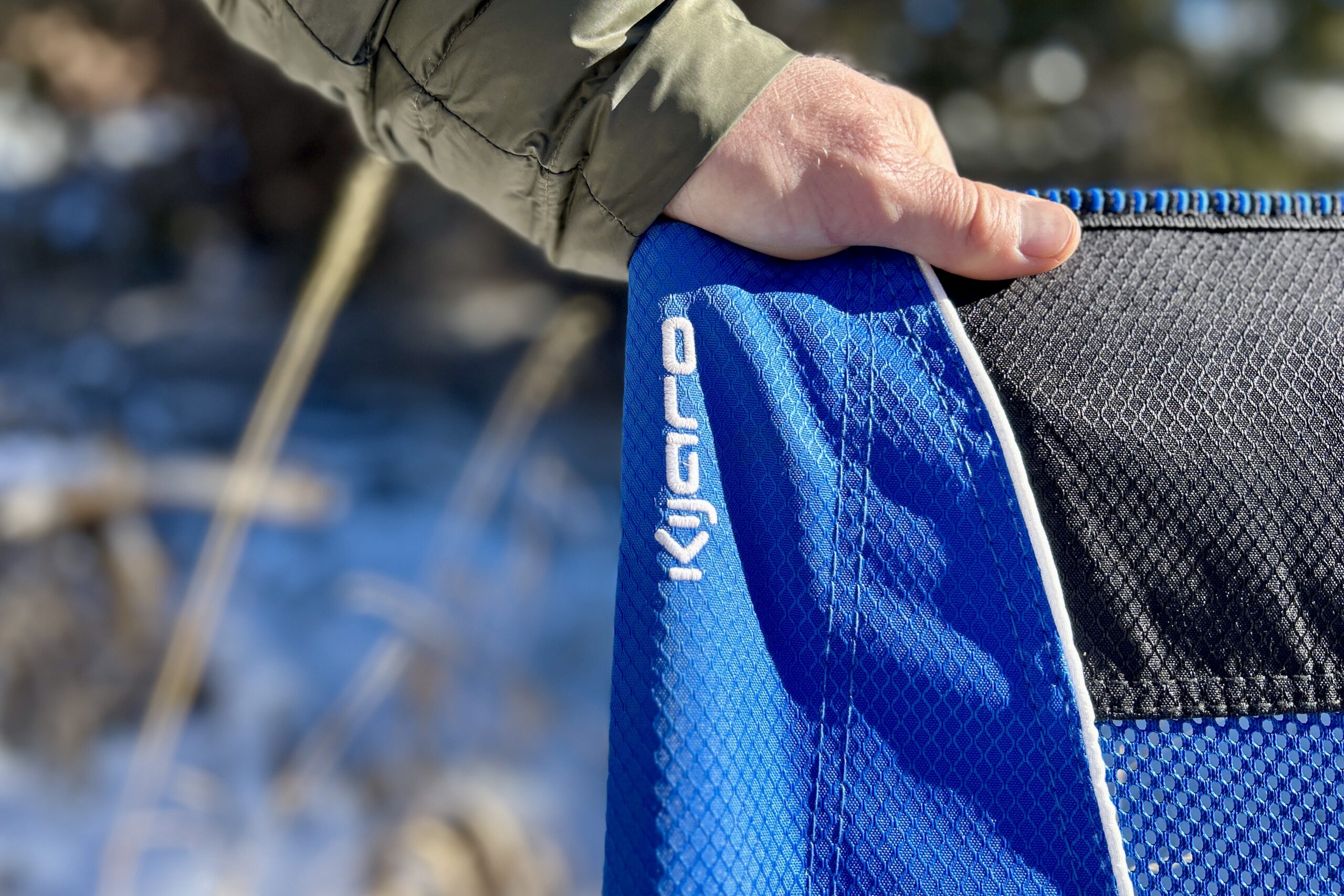Close up of a person's hand on the backrest of a camping chair with the logo visible.