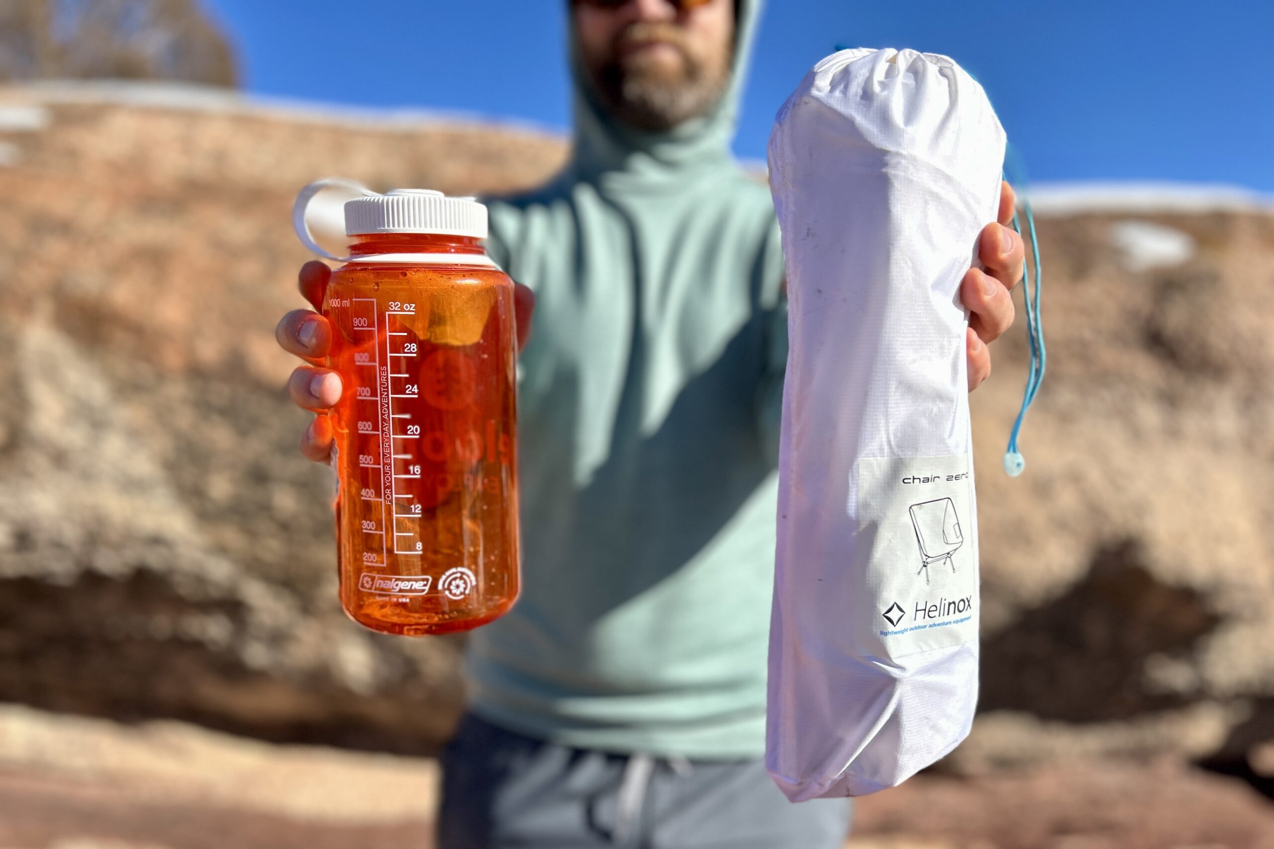 A person holds out a small camping chair in its drawstring bag next to a Nalgene for size reference.