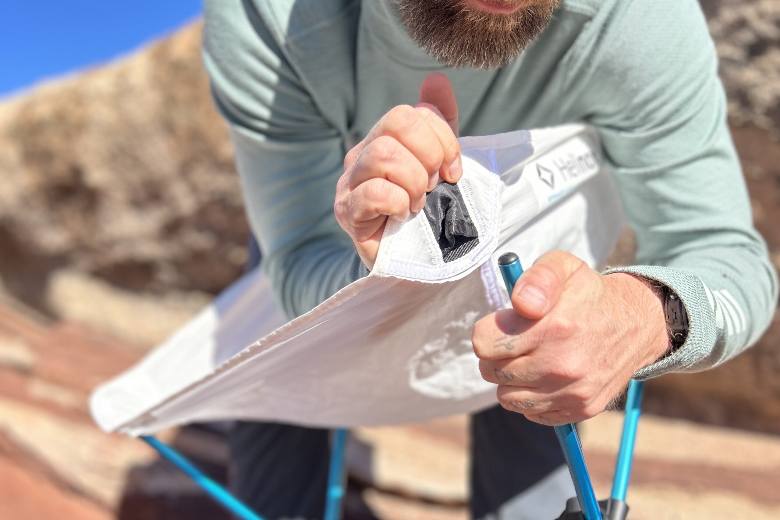 Close up of a person putting the pole of a camping chair frame into the fabric of the seat.