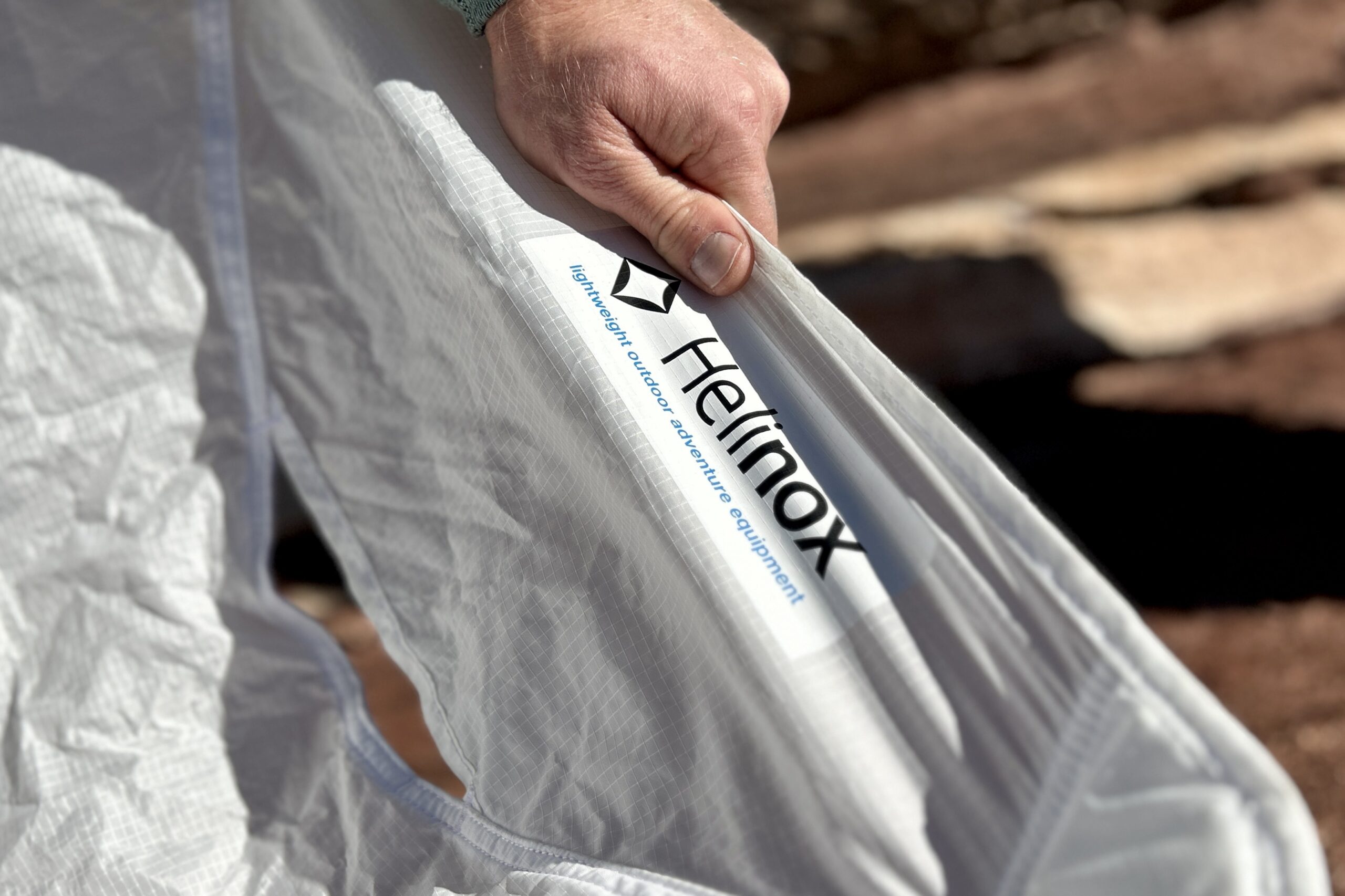 Close up of a hand holding onto the thin white fabric of a camping chair with the logo visible.