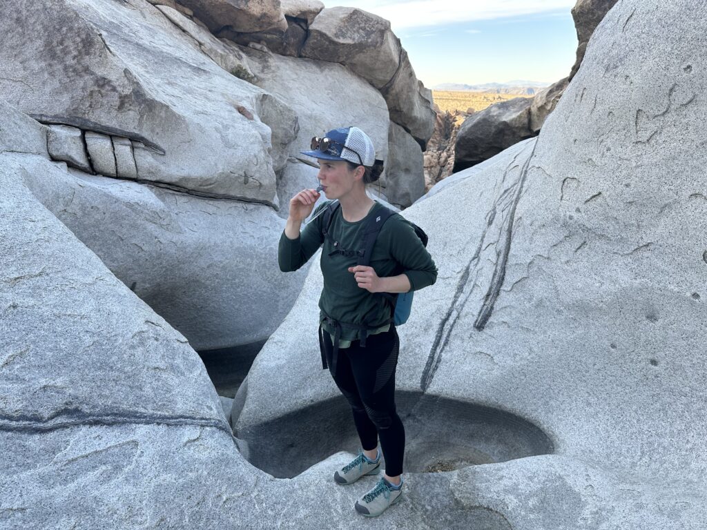 A hiker drinks from a hydration hose while standing in a water-carved granite canyon in the desert.