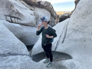 A hiker drinks from a hydration hose while standing in a water-carved granite canyon in the desert.