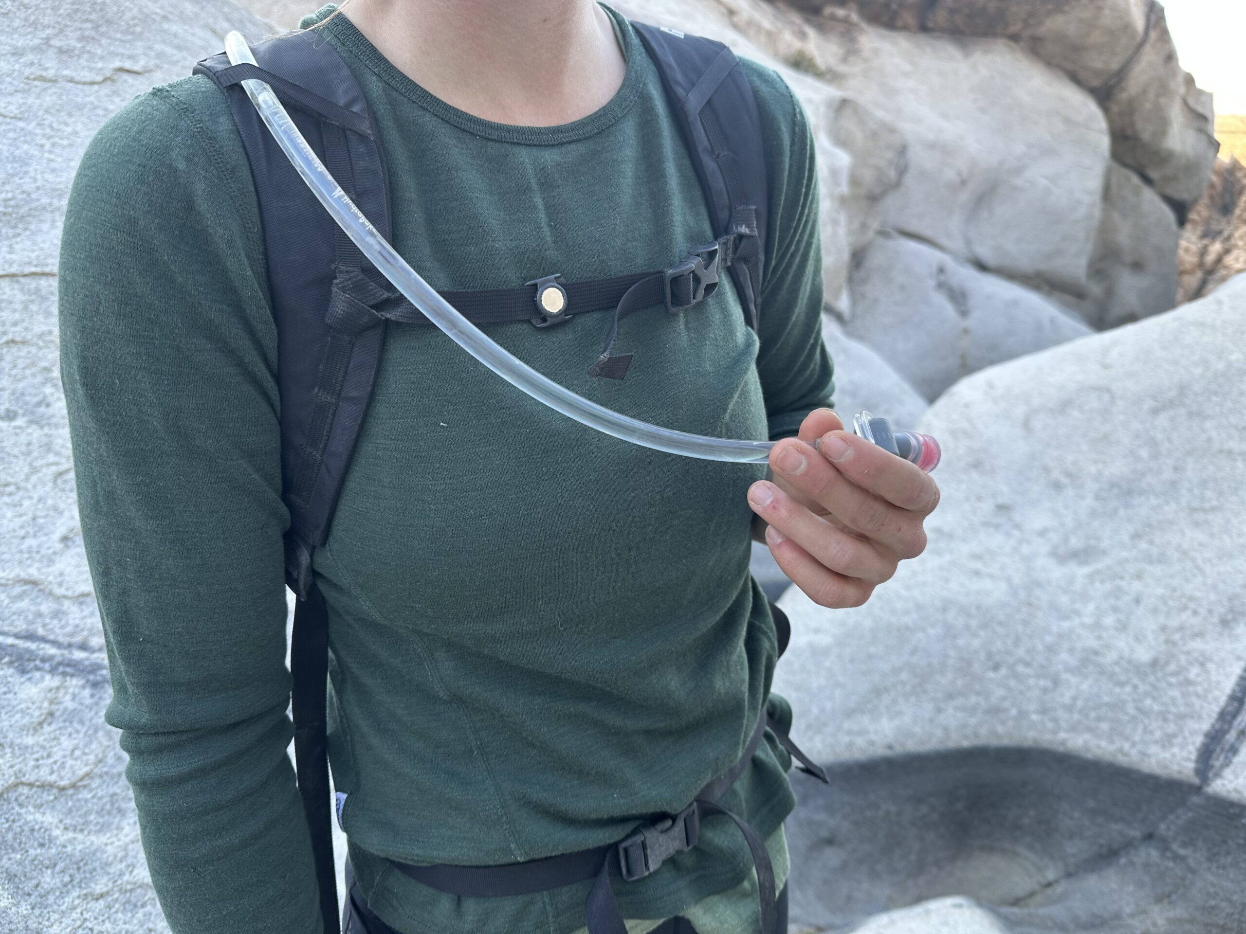 Close up photo of a hiker's chest showing the sternum strap magnet that secures the hydration hose while hiking.