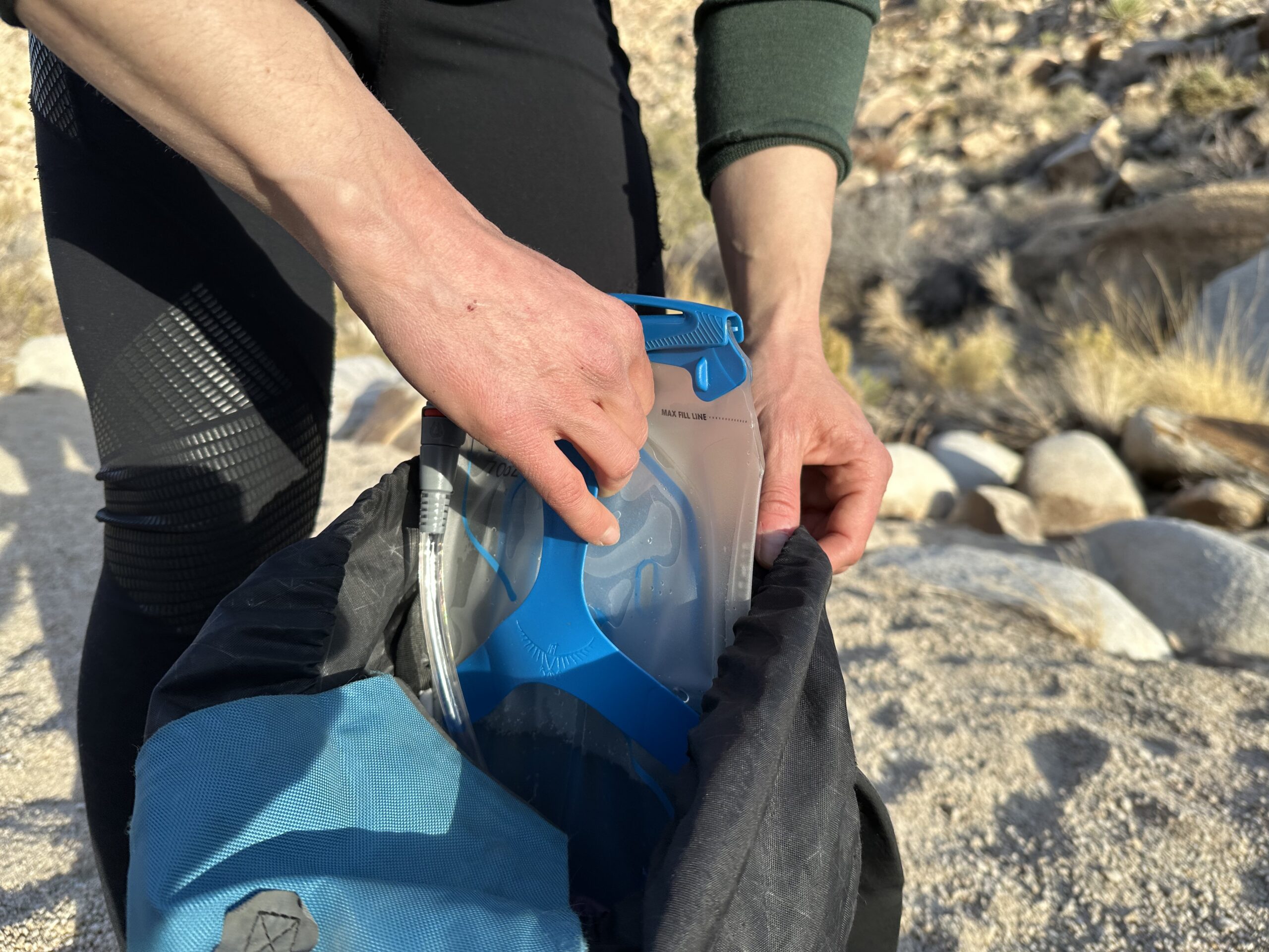 Close up of a hiker using the rigid plastic handle to load the Osprey Hydraulics Reservoir into her backpack.