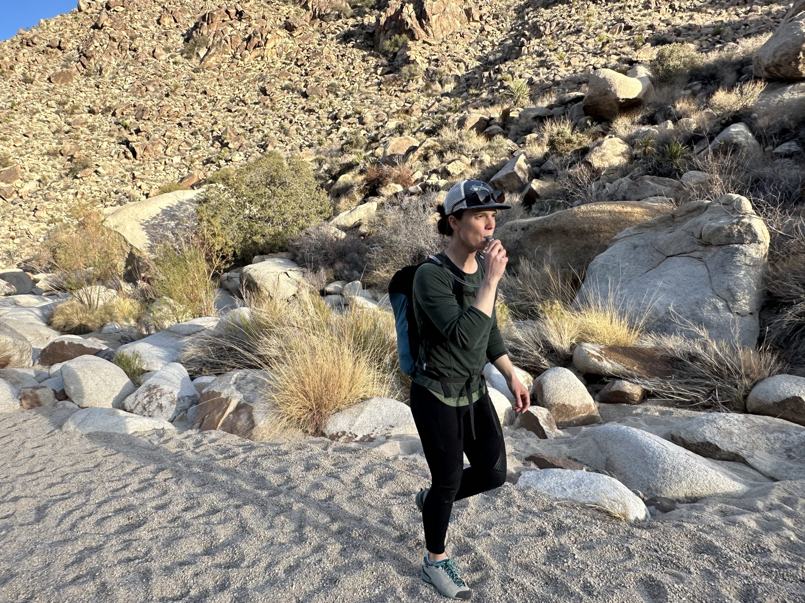A hiker drinks from a hydration hose while walking through a sandy wash near the top of Rattlesnake Canyon in Joshua Tree National Park
