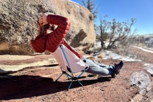 A man relaxes with his legs out and hands behind his head on a small backpacking chair.