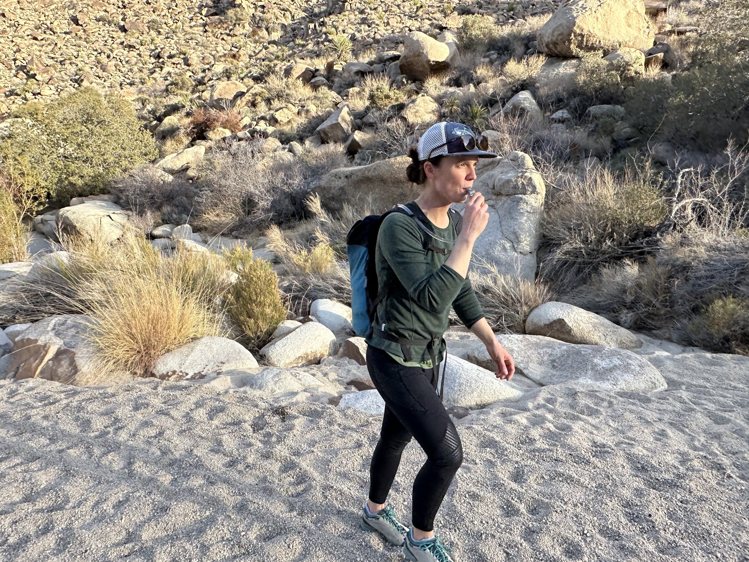 A hiker walks through Rattlesnake Canyon in Joshua Tree National Park while drinking from a hydration bladder.
