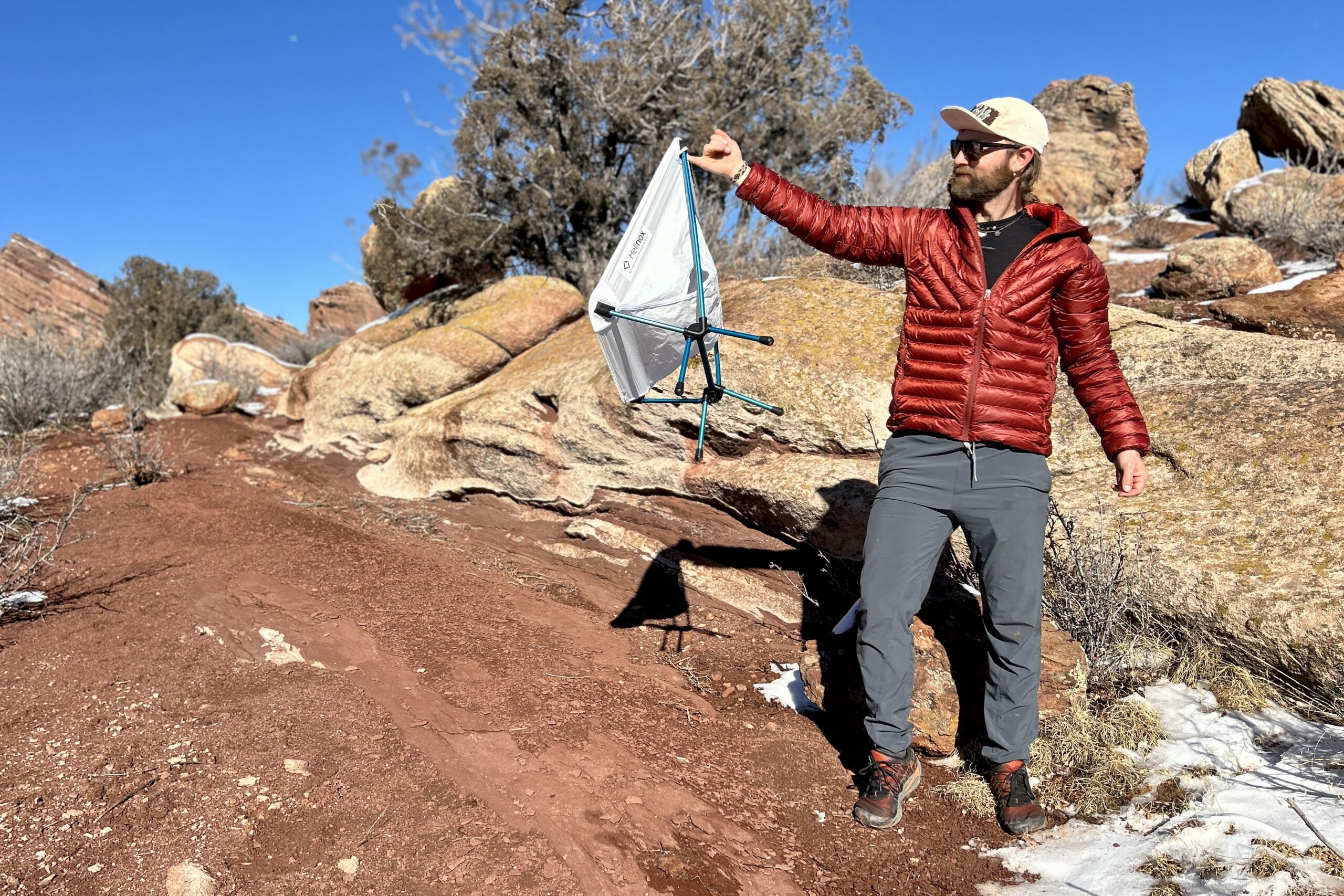 A man holds out a small backpacking chair with one pinky in a desert setting.