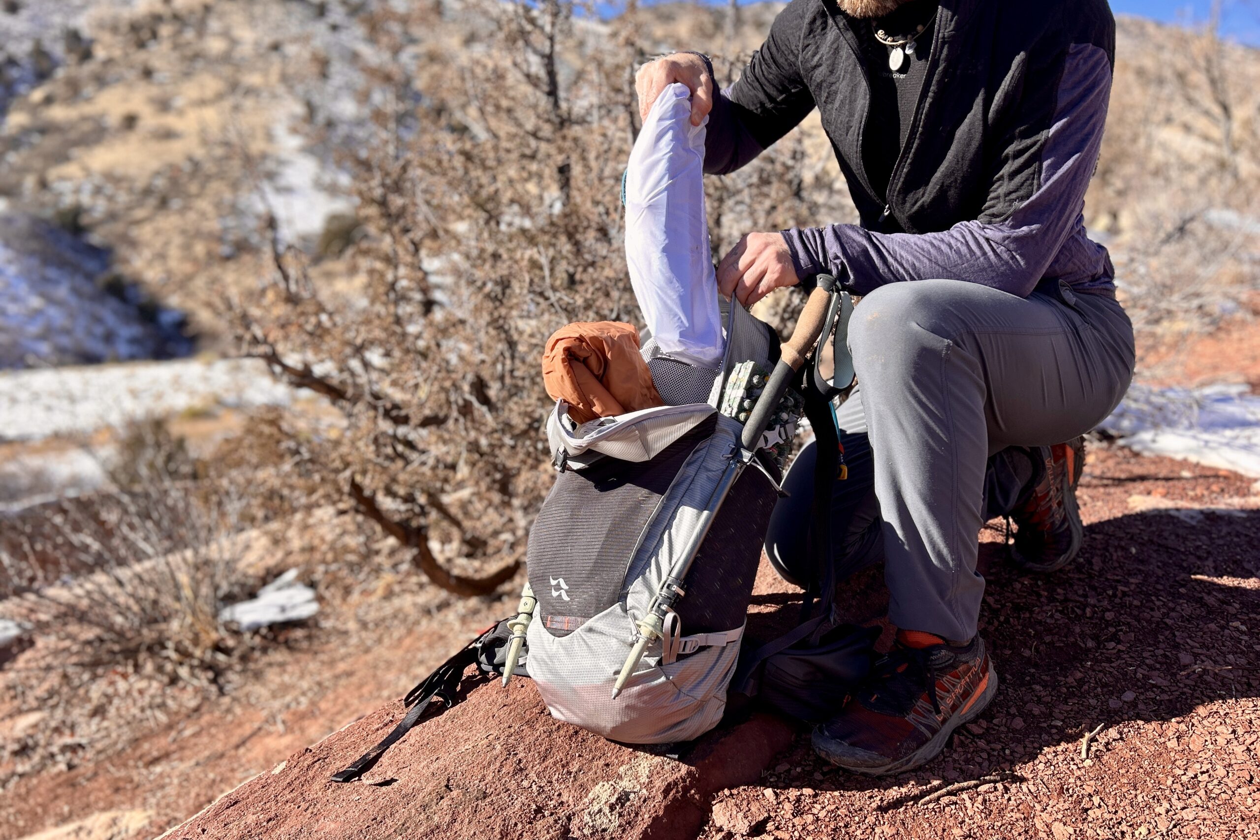 A person puts a small backpacking chair into a backpack for carrying.