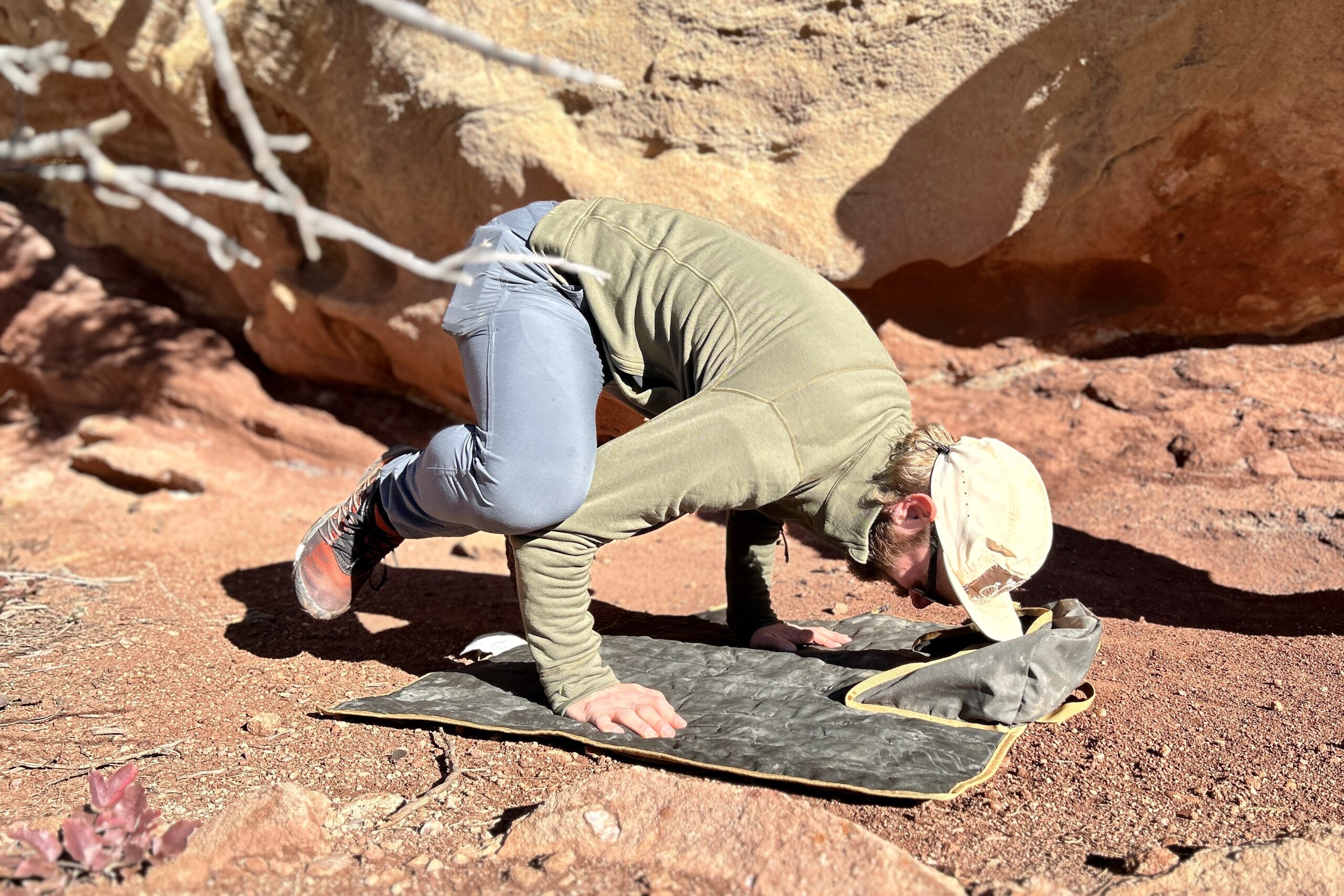 A man does a yoga pose on the flat carrying case of a camping chair.