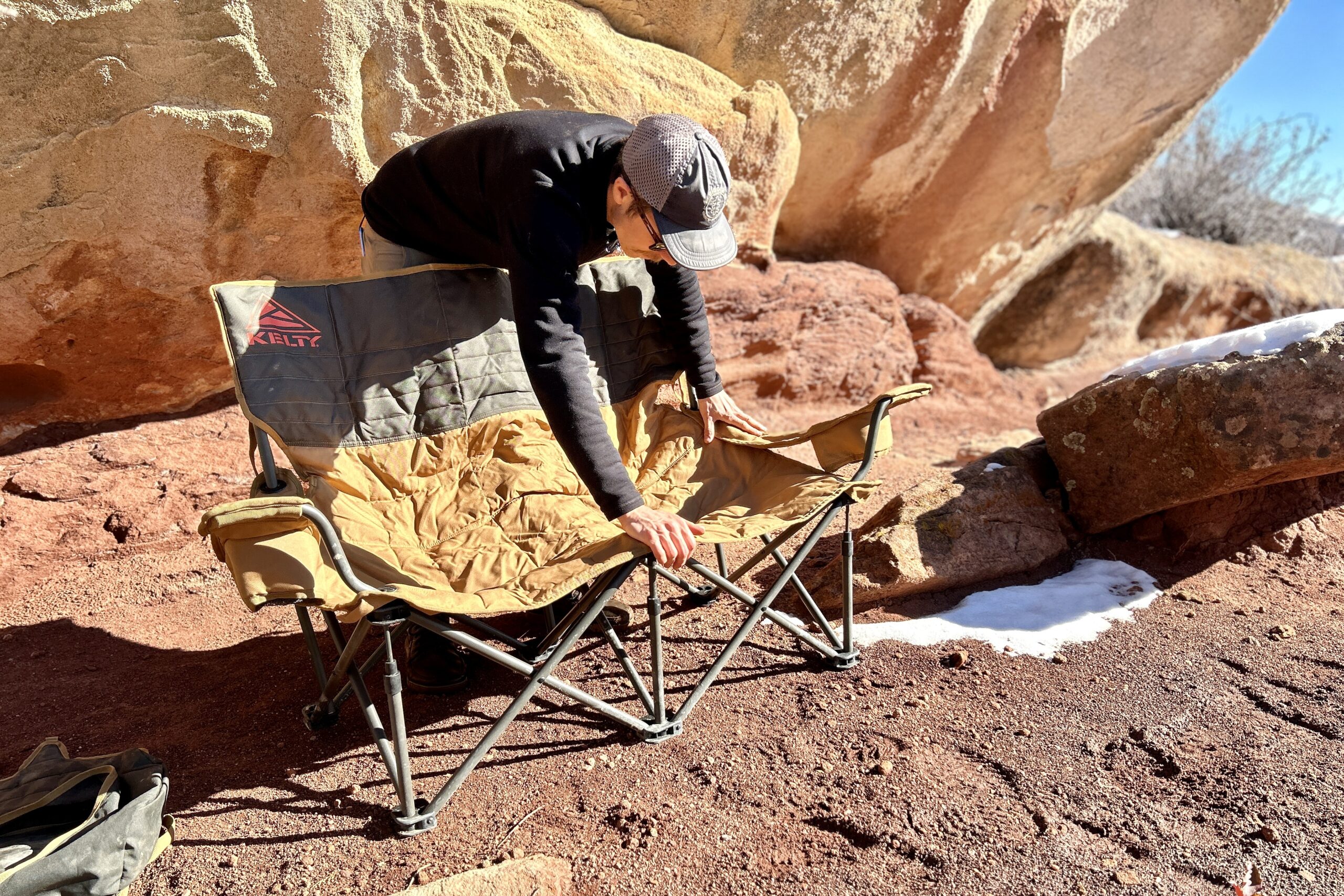 A man sets up a two person camping chair in a desert place.