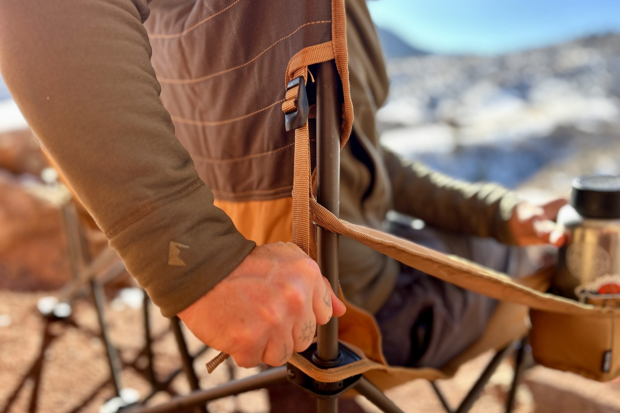 A person tightens the adjustable nylon strap of the armrest on a camping chair.