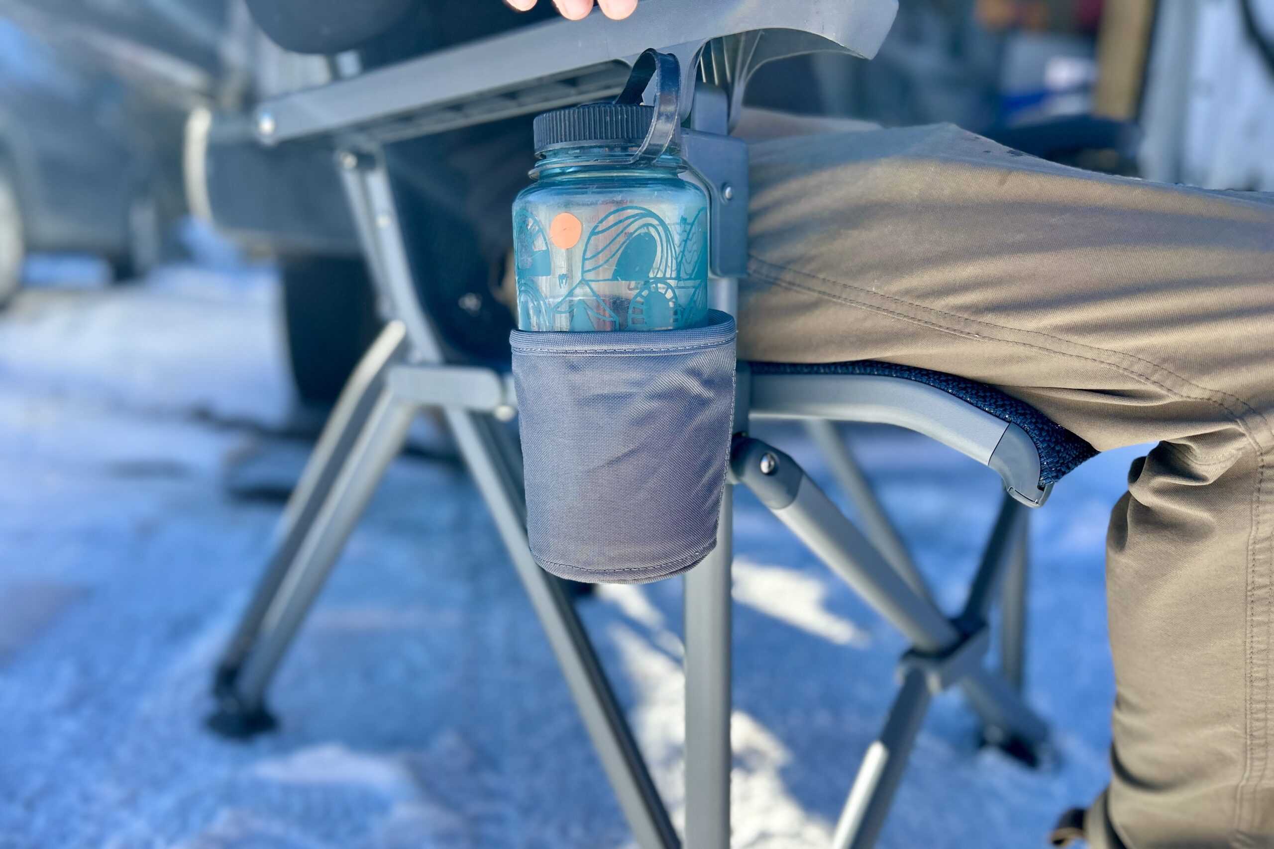 Close up of a Nalgene water bottle in the fabric cupholder of a camping chair.