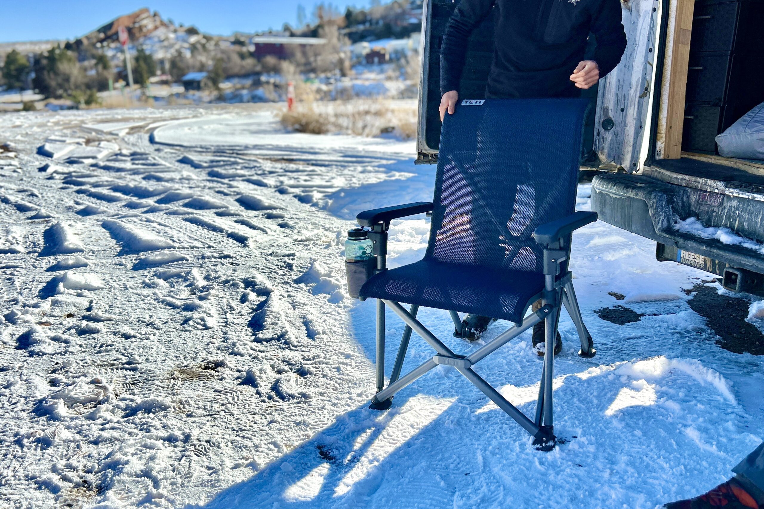 A person holds onto the back of a camping chair in a parking lot.
