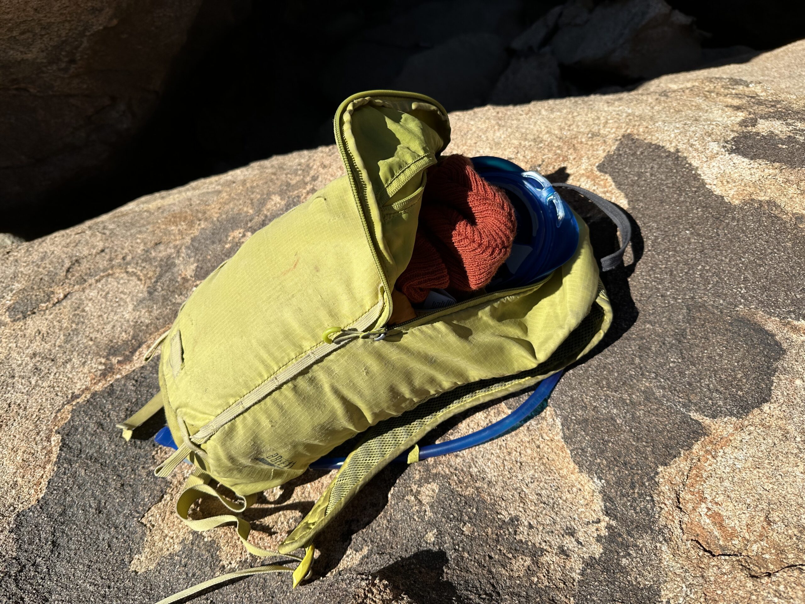 A close up photo of the CamelBak Crux tucked into the hydration sleeve of a small yellow daypack that's sitting on a large granite rock.