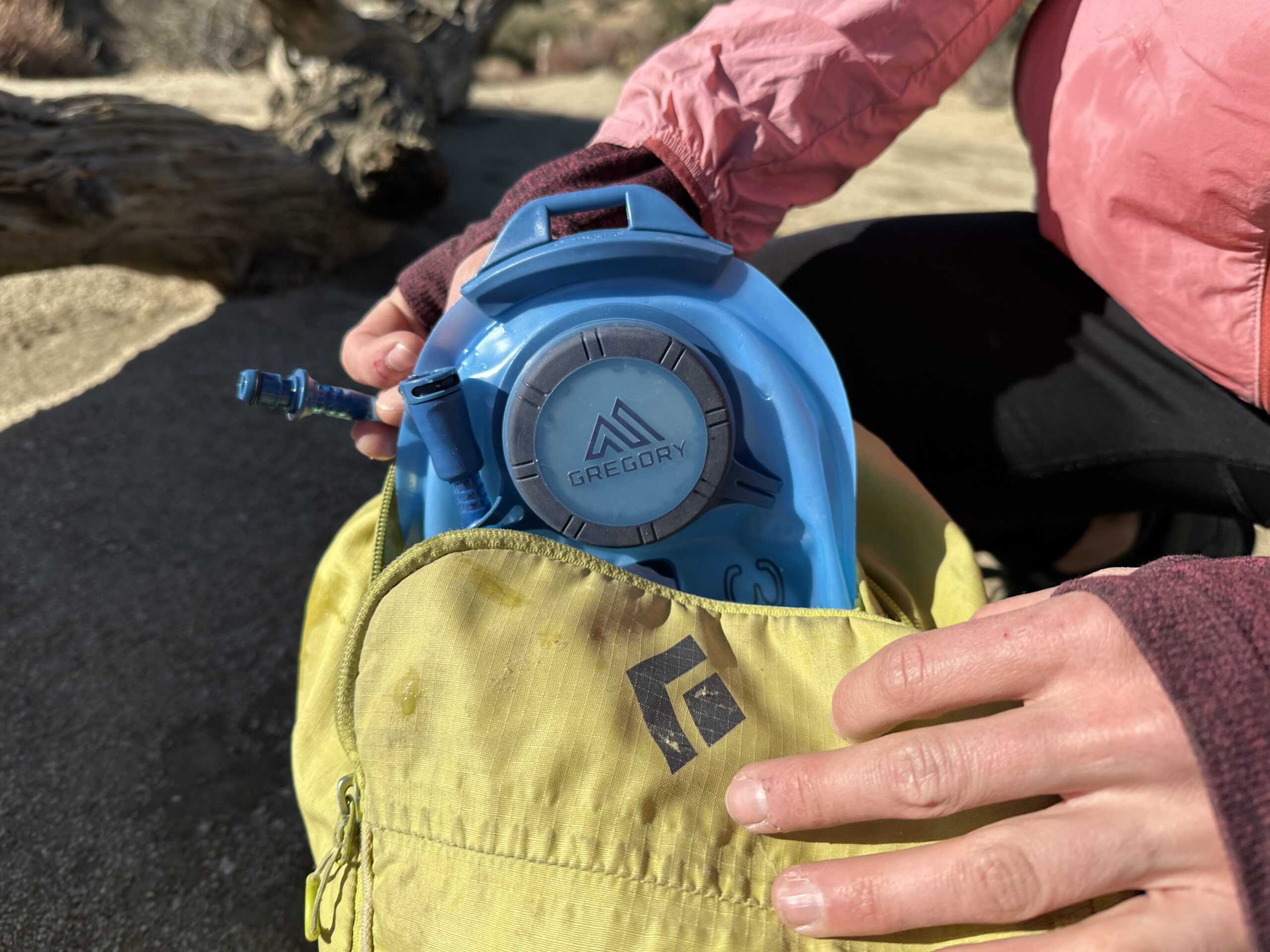 A close up image of a hiker reloading a hydration bladder back into her backpack, showing the hose quick release near the top of the bladder.