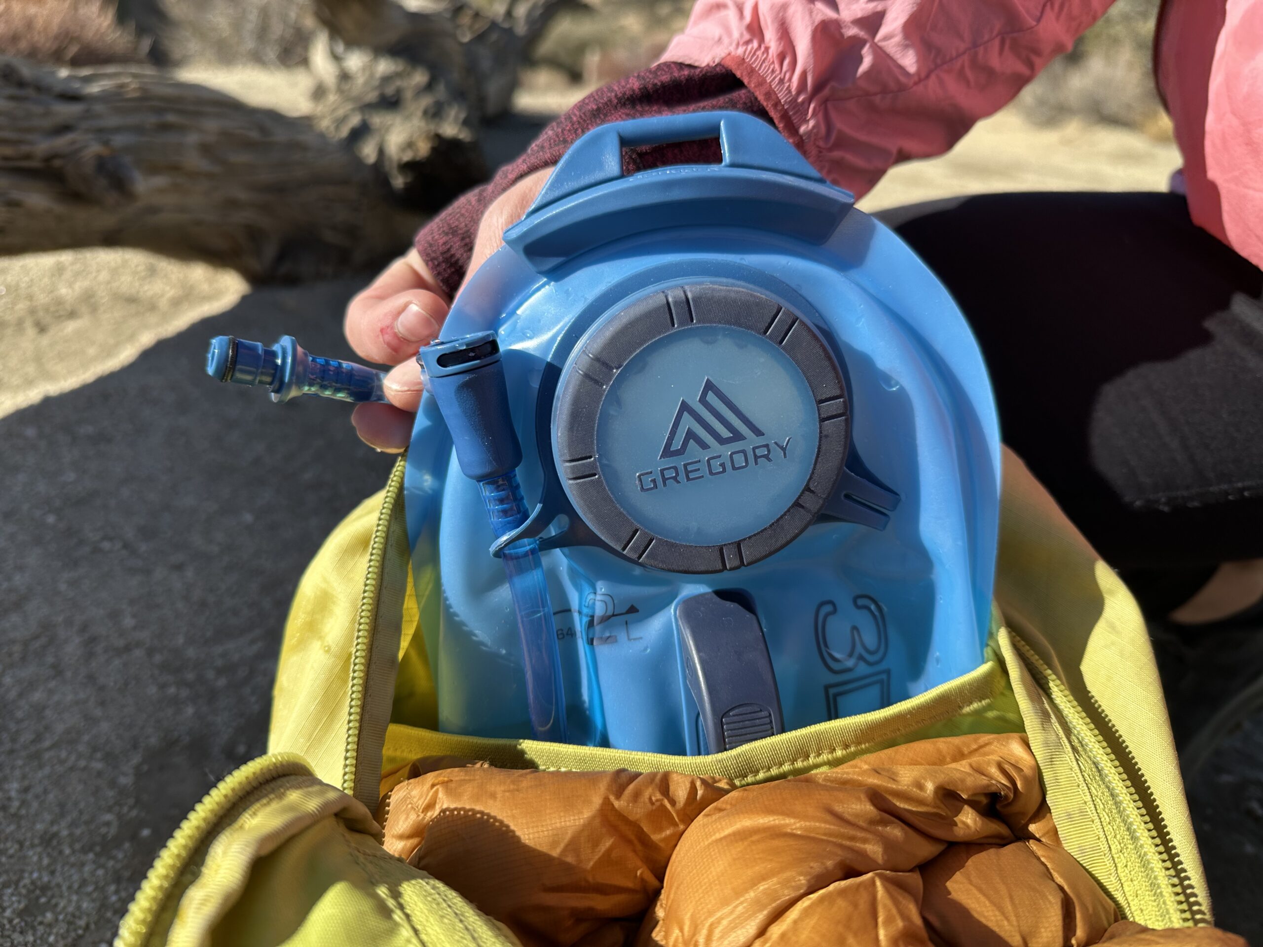 A close up image of a hiker re-loading a Gregory 3D Hydro Reservoir back into the hydration sleeve of a small day pack.