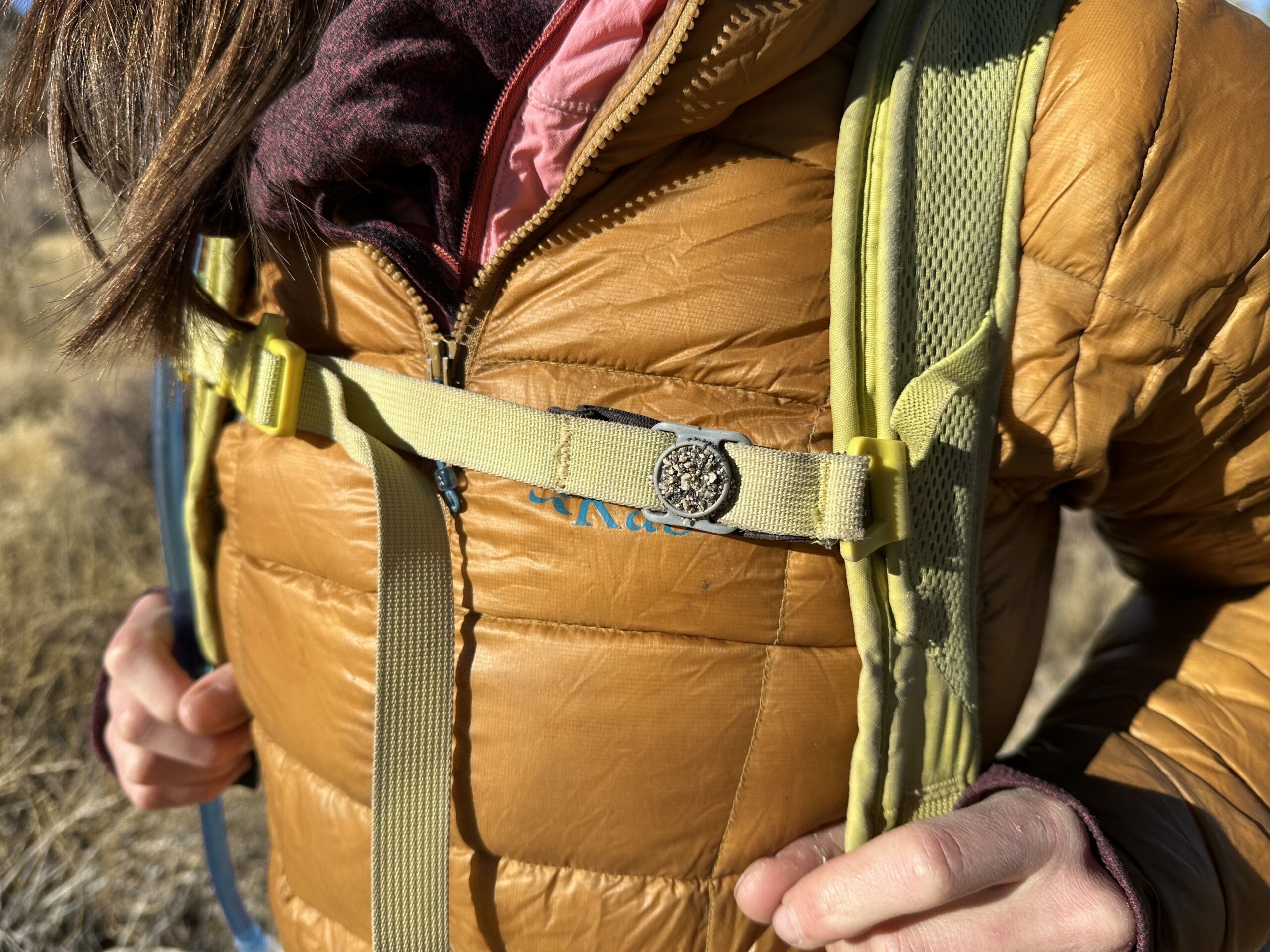 A close-up image showing sand sticking to the sternum strap magnet on a hiker's backpack.