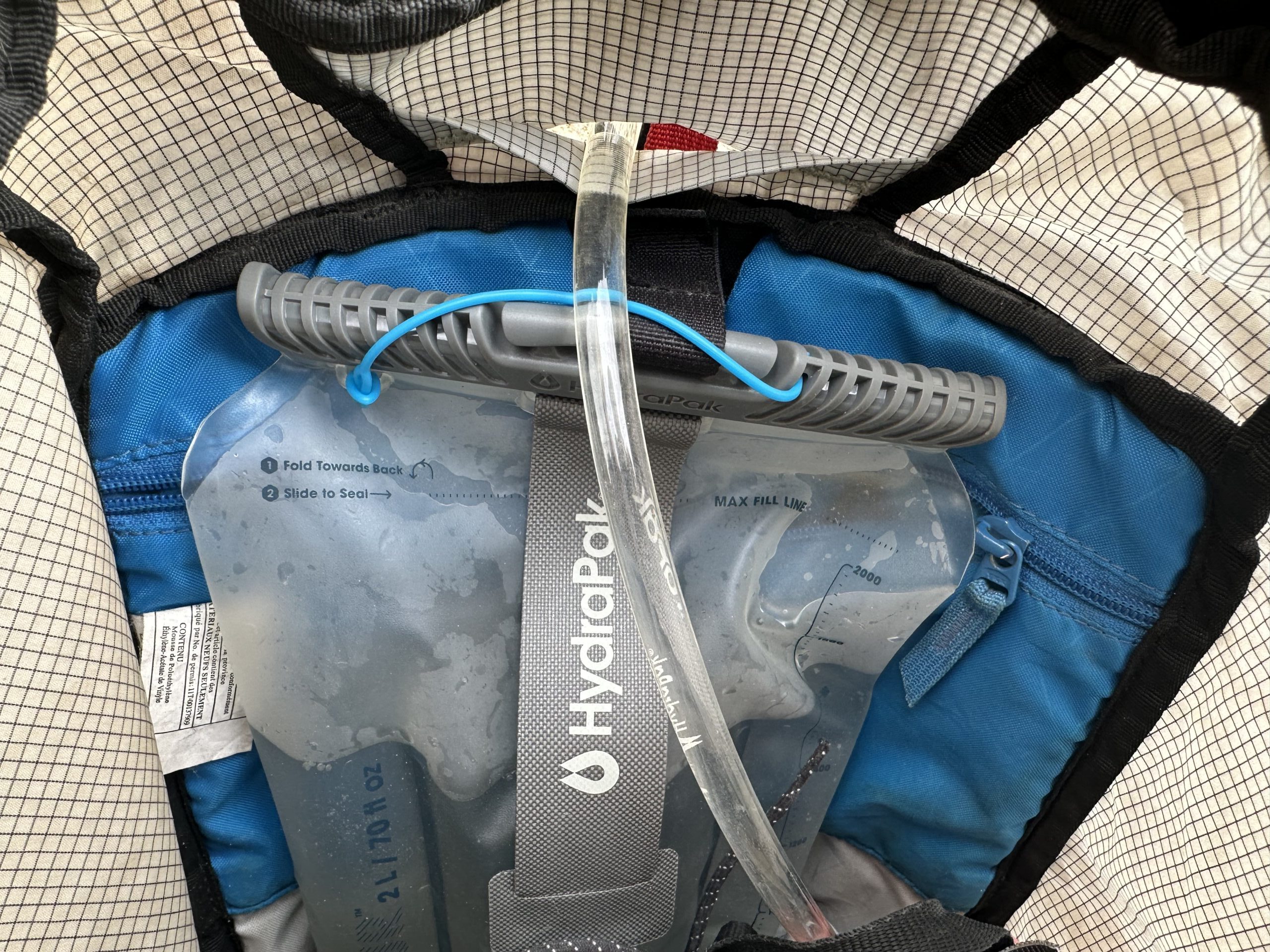Inside of a backpack showing the HydraPak Contour suspended by a velcro strap, with the hydration hose running out of a hole in the backpack.