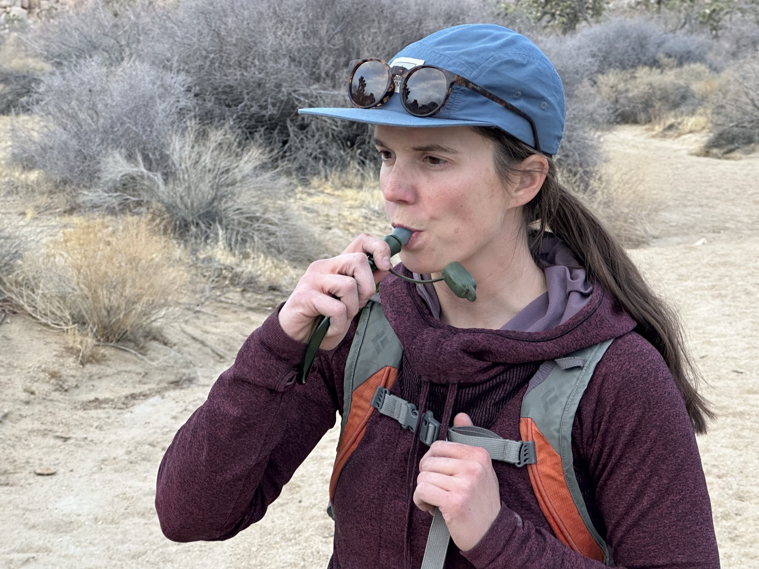 Close up photo of a hiker drinking out of the Cherainti Bladder's bite valve. Background is a sandy wash