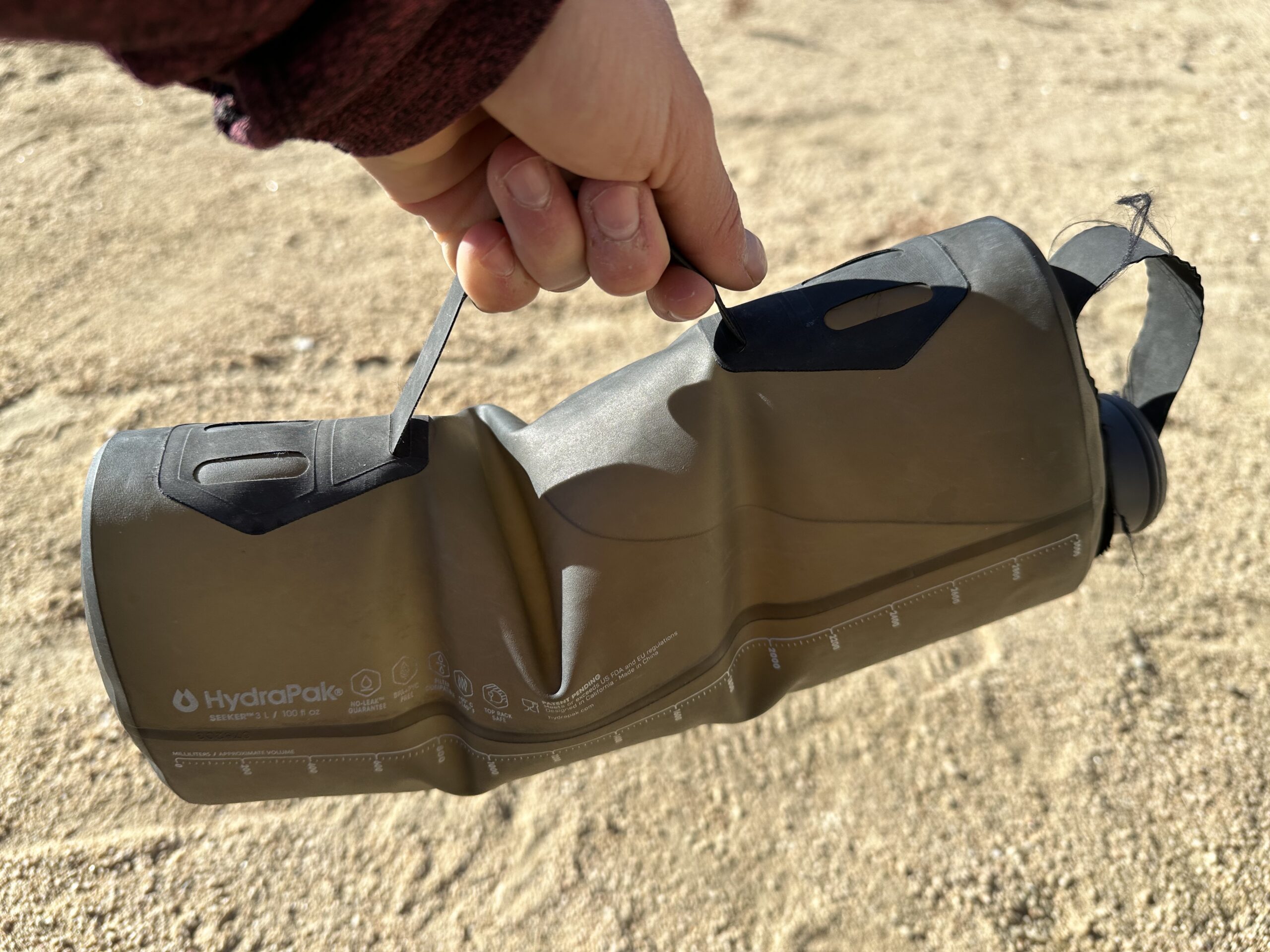 Close-up photo of a hand holding the handle on the side of the HydraPak Seeker water bag. The bag is full of water.