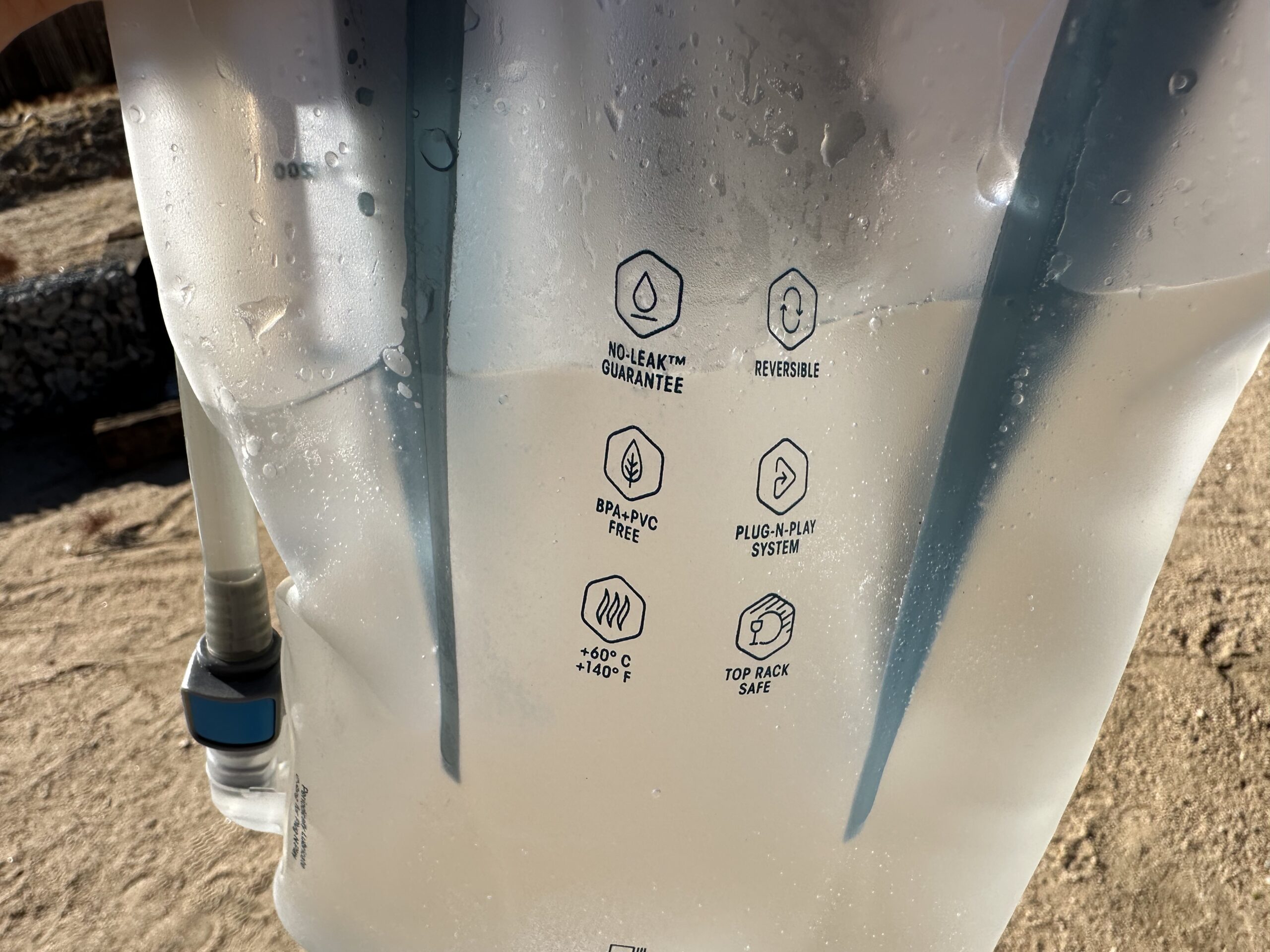 A close-up of the HydraPak Contour, with some water inside. On the bladder are words that read "No leak Guarantee," "Reversible," "BPA +PVC Free," "Plug-n-play system," "+60C +140F," "Top Rack Safe."