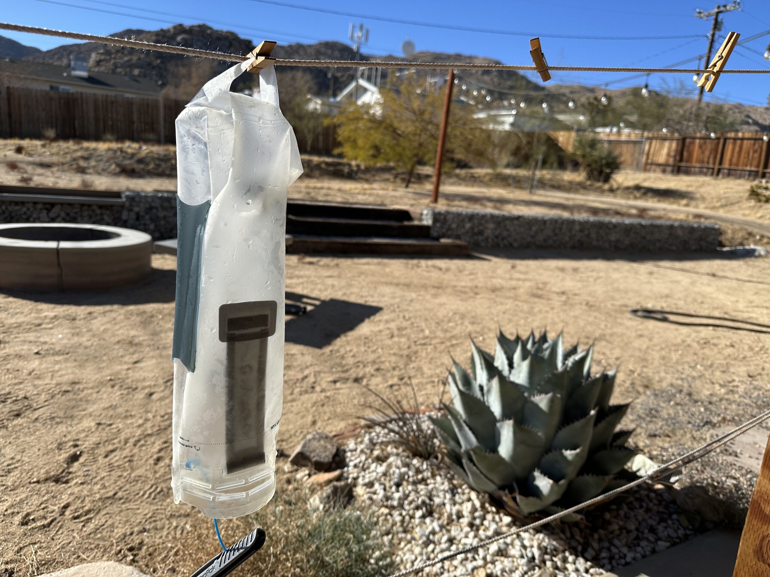 The HydraPak Contour bladder is turned inside out and hanging from a clothesline to dry. The background is a sunny backyard in the desert.