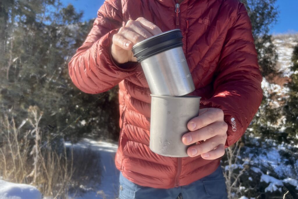 A hiker nests the two pieces of the insulated mug together with a snowy background.