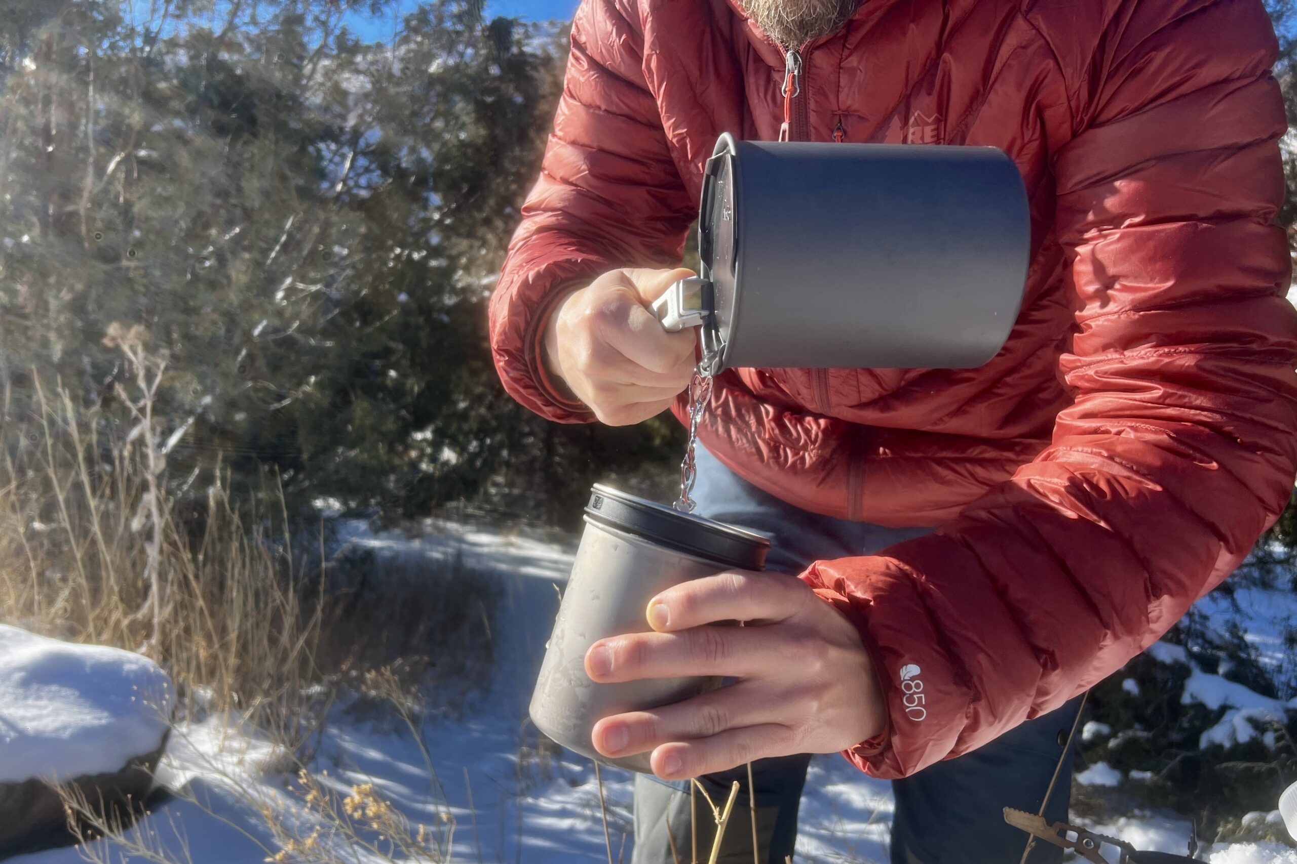 A hiker pours water from the pot into the insulated mug of the soto thermostack combo against a snowy desert background.