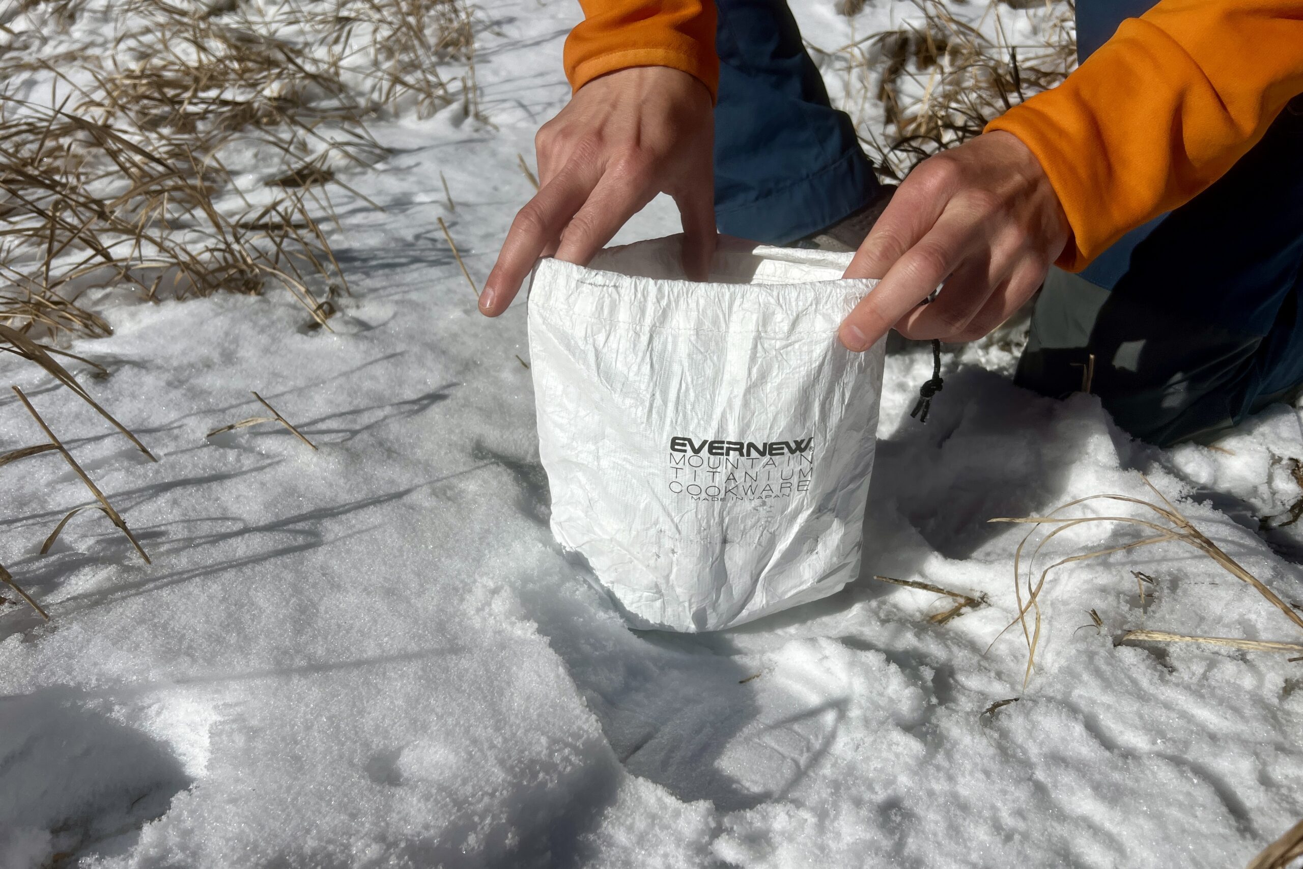 A hiker holds open the stuff sack of the evernew pasta pot against a snowy background.