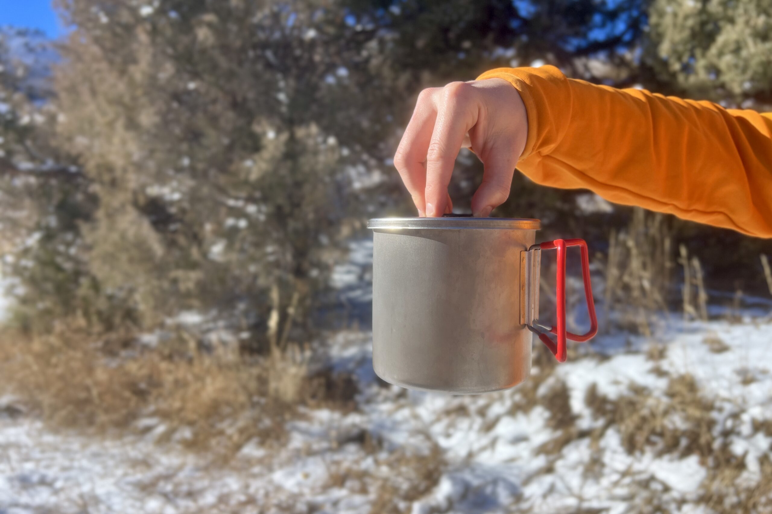 A hand holding the Evernew pasta pot from the lid with a snow background.