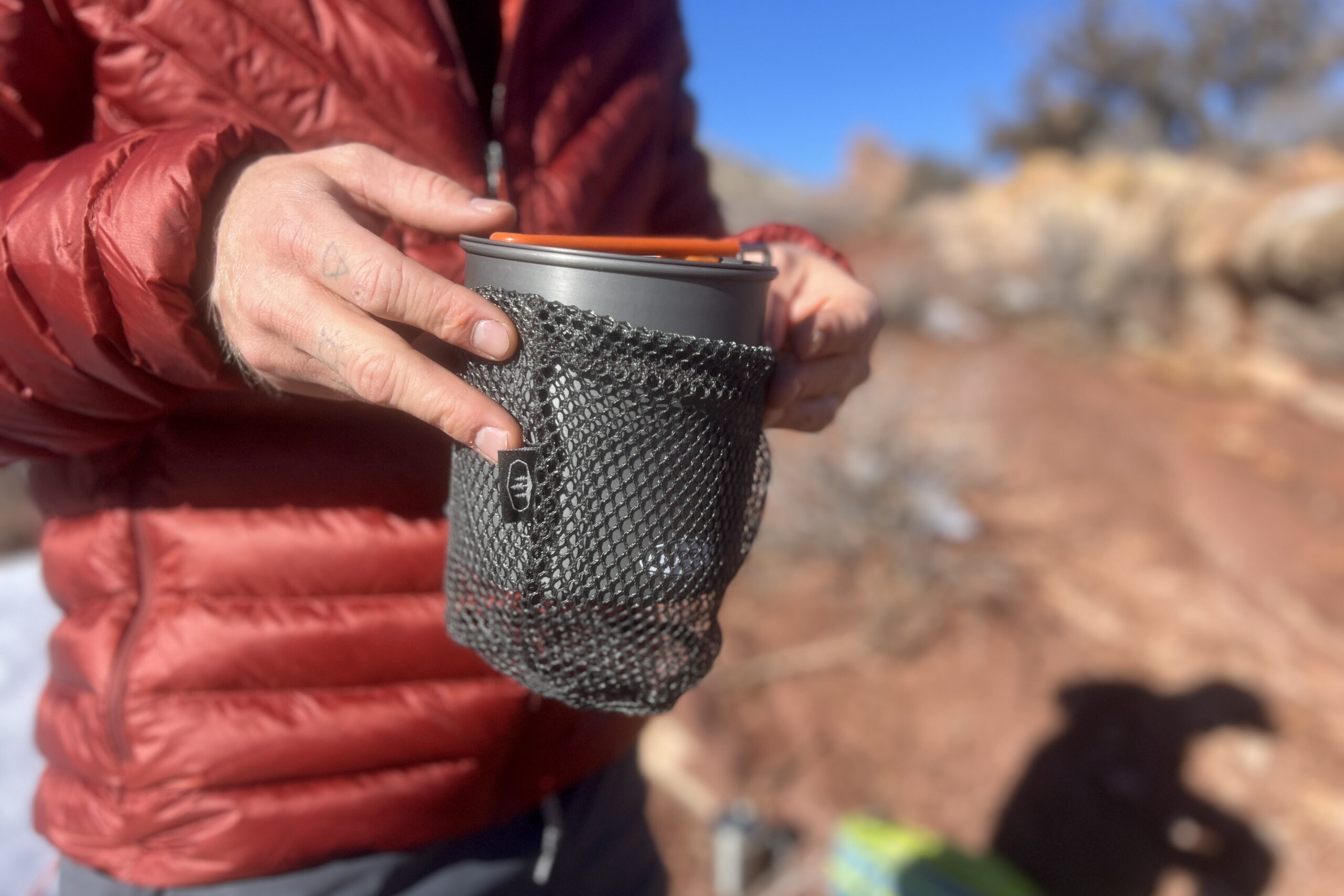 A hiker packs the gsi halulite boiler into its mesh stuff sack with red rocks in the background.