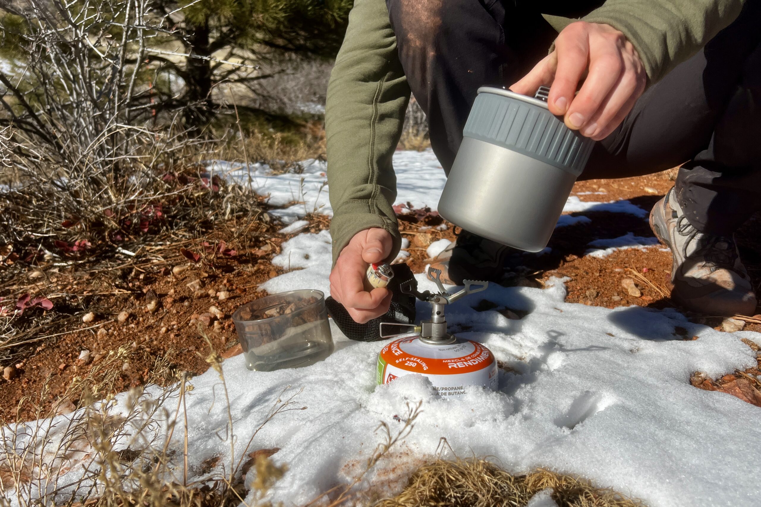 a hiker prepares to light a backpacking stove while holding the msr trail mini solo. deserty background