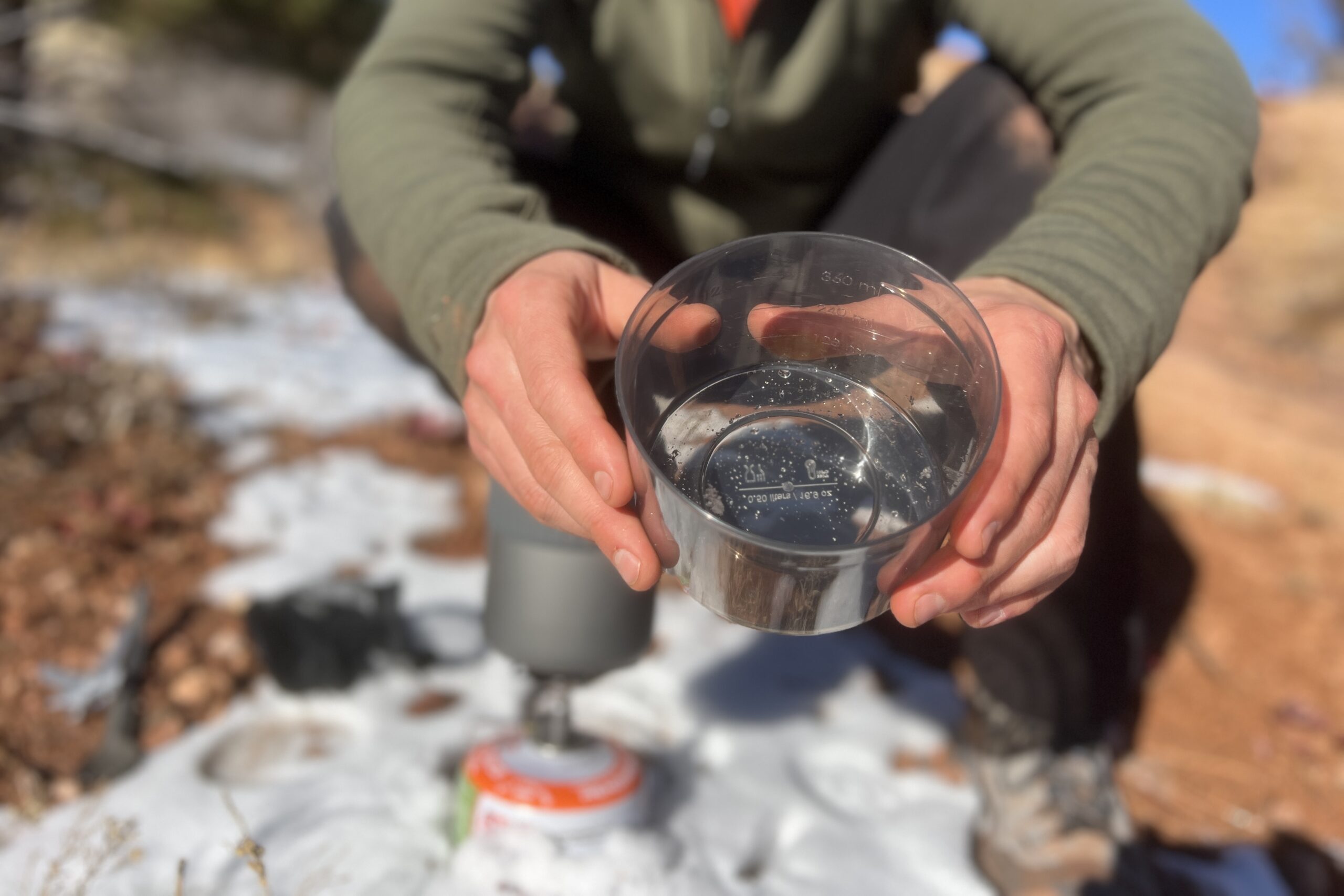 A hiker shows the plastic cup of the msr trail mini solo to the camera against a snowy background.