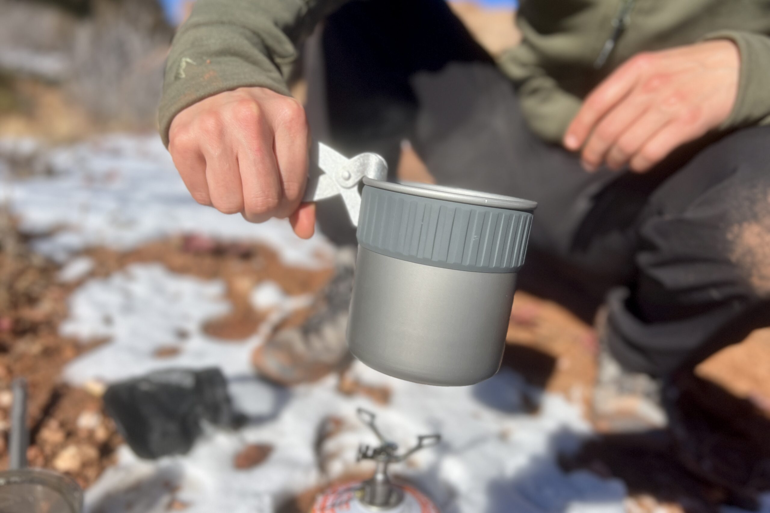 A hiker holds the msr trail mini solo with the included pot lifter against a snowy desert background.