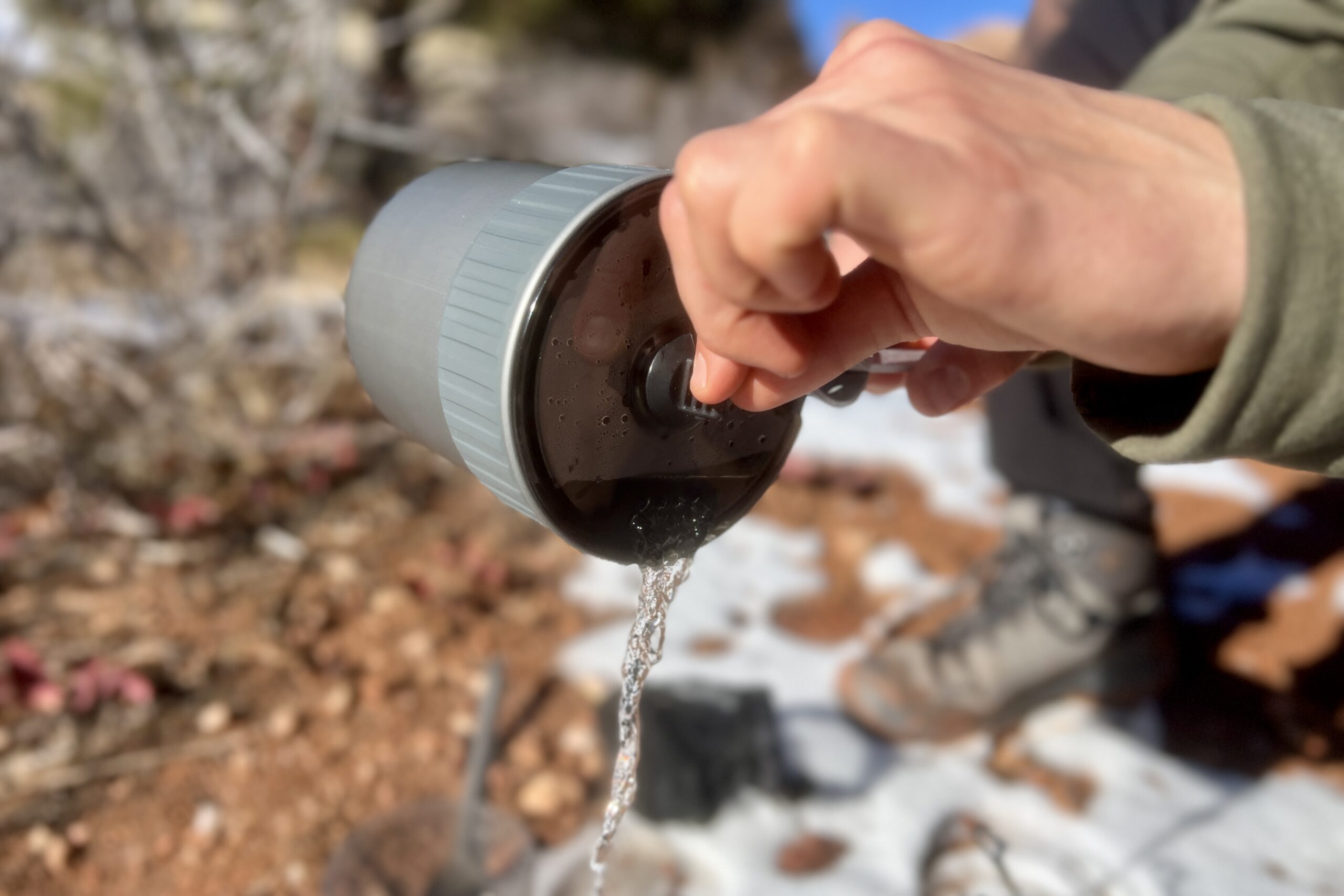 A hiker pours water through the drain holes of the msr trail mini solo's lid with a desert background.
