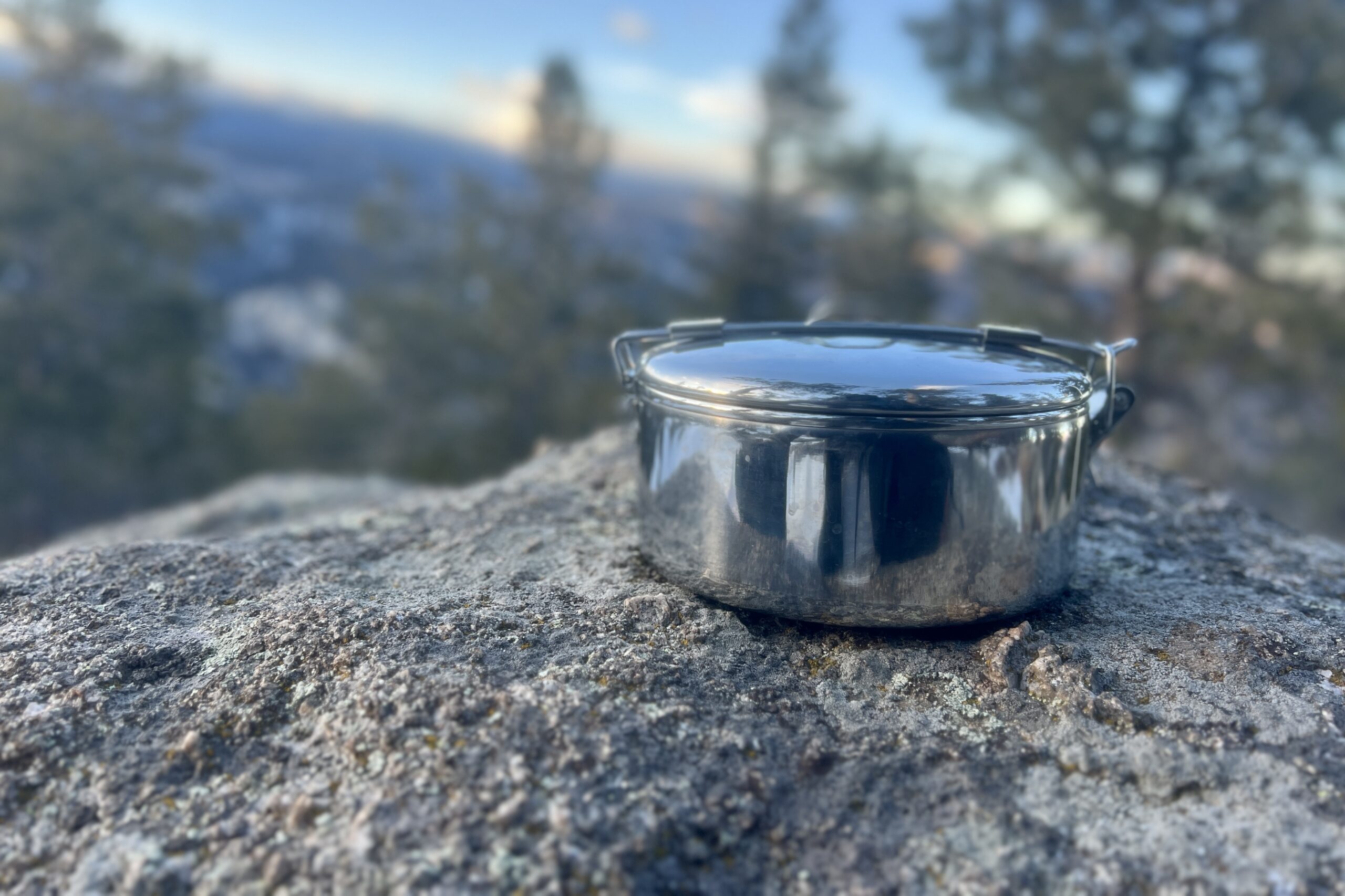 A steel backpacking pot with a foldable handle sitting on a rock
