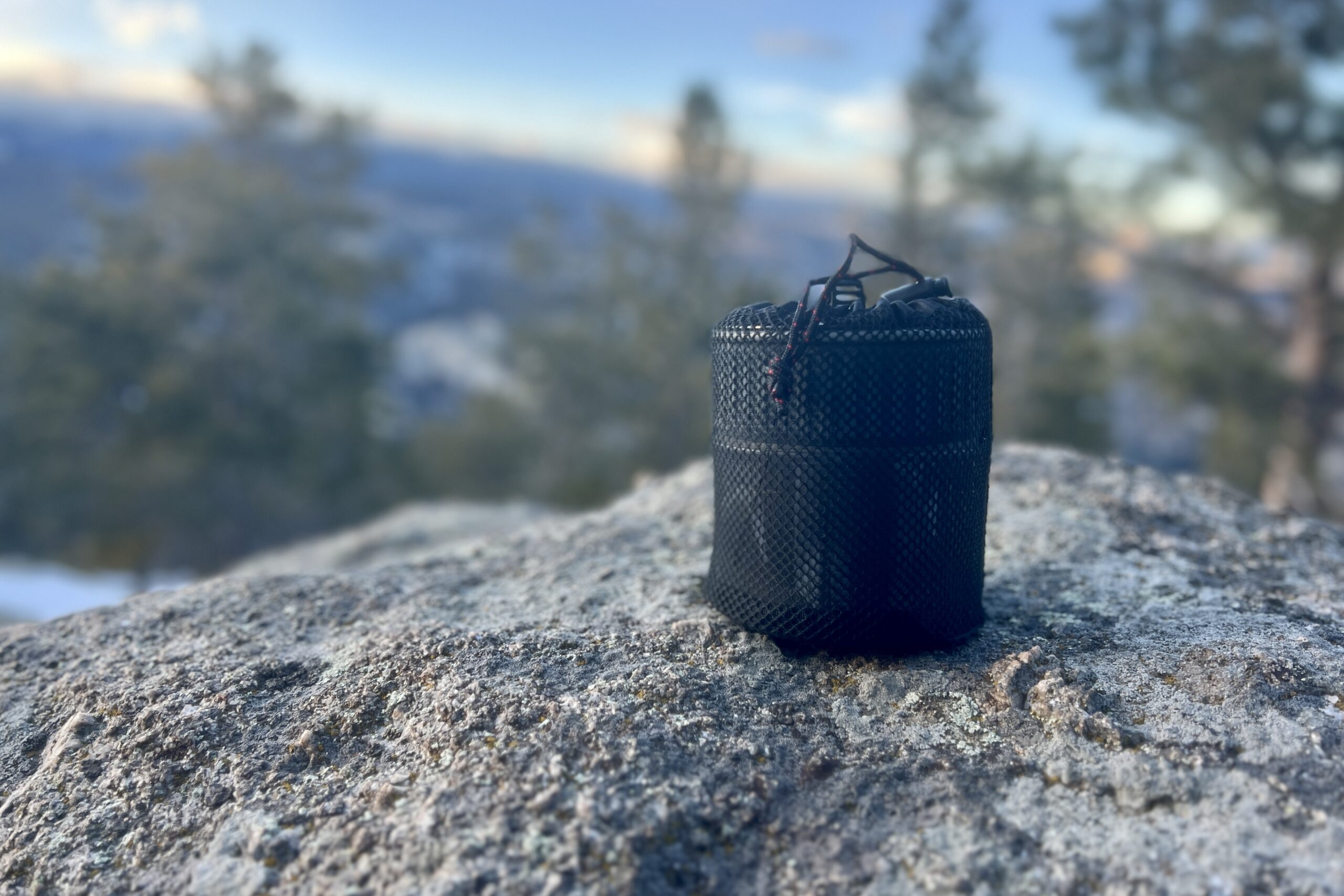 The msr trail mini solo packed into its stuff sack and sitting on a rock against a blurry forest background.